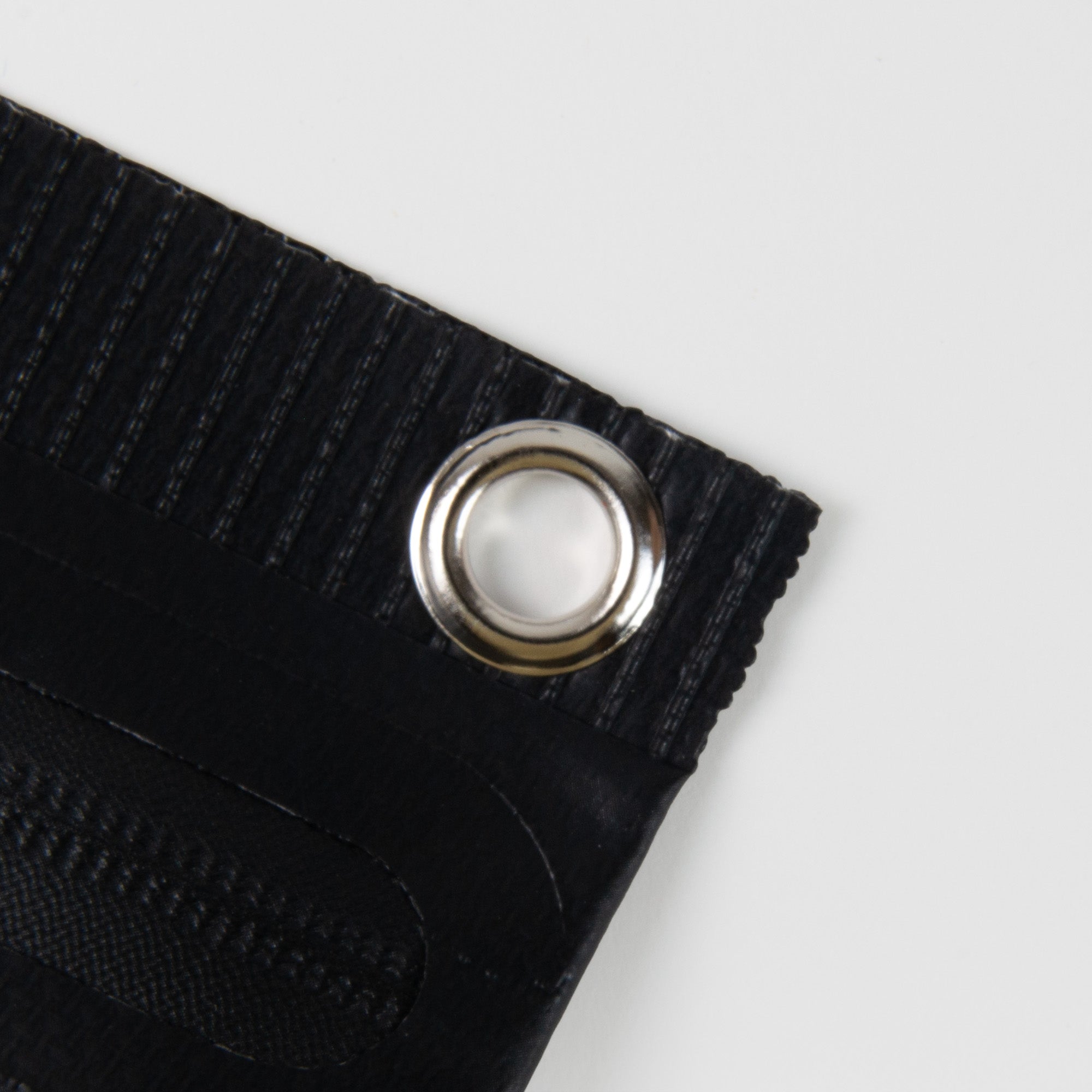 Nahaufnahme der schwarzen, strukturierten Penco Tarp Pouch S mit einer silbernen Metalltülle in der Ecke vor einem schlichten weißen Hintergrund.