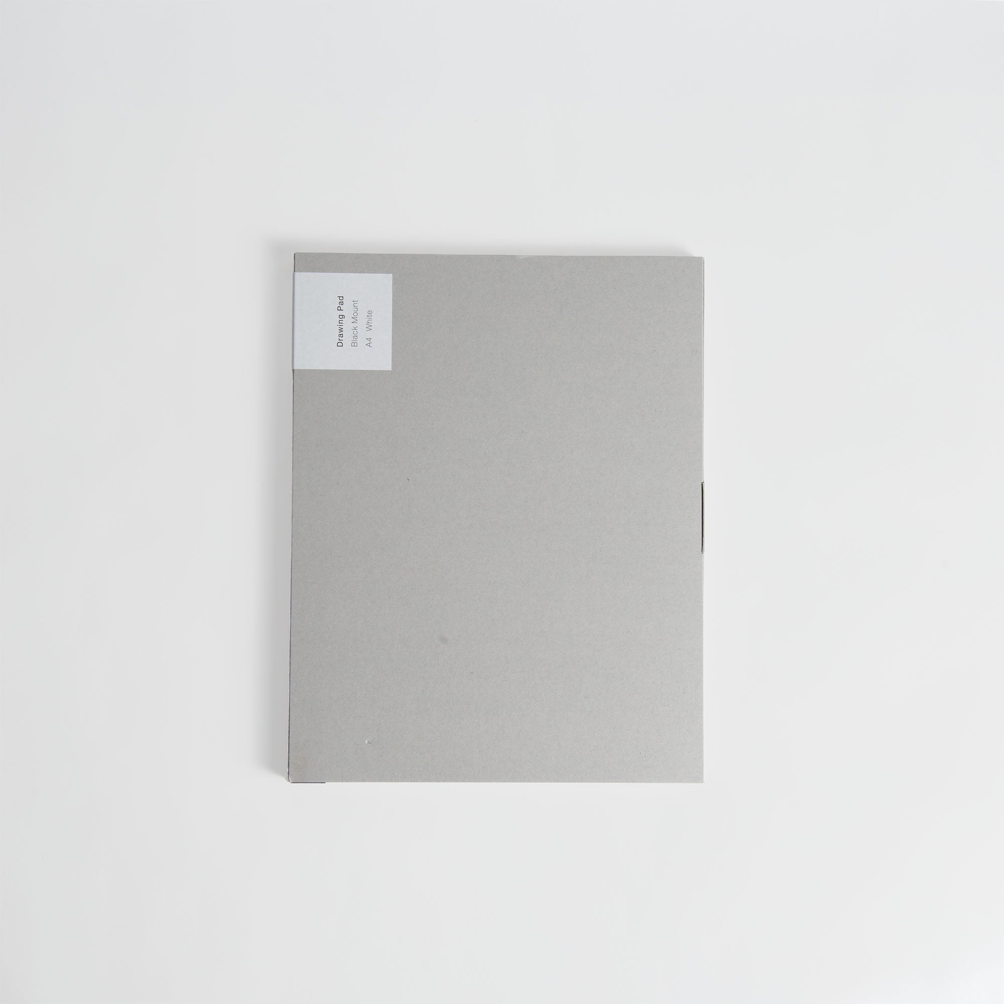 Ein geschlossener ITO Bindery Drawing Pad Black Mount von ITO Bindery, grau mit einem kleinen weißen Etikett in der oberen linken Ecke, liegt auf einem schlichten weißen Hintergrund.