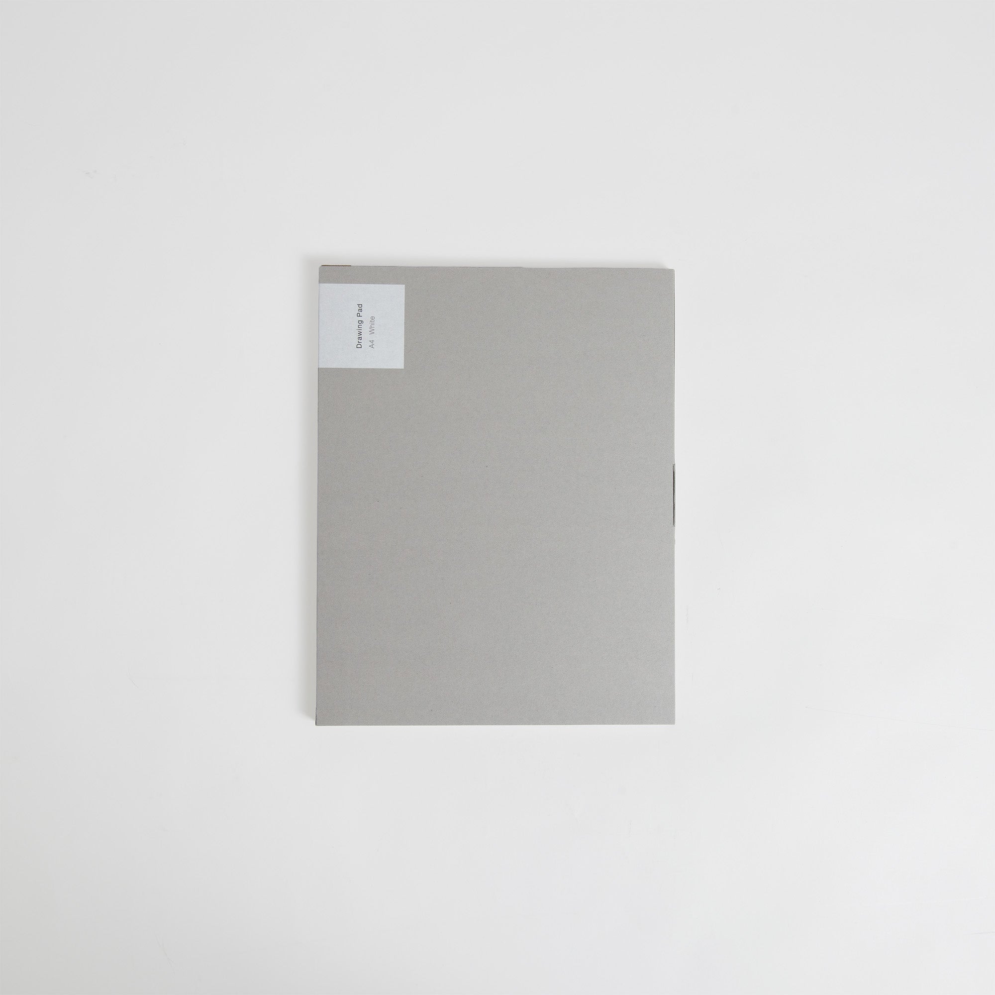 Eine geschlossene graue Mappe mit einem kleinen weißen Etikett in der oberen linken Ecke liegt auf einer schlichten weißen Oberfläche und erinnert an den minimalistischen Stil des ITO Bindery Drawing Pad White von ITO Bindery.