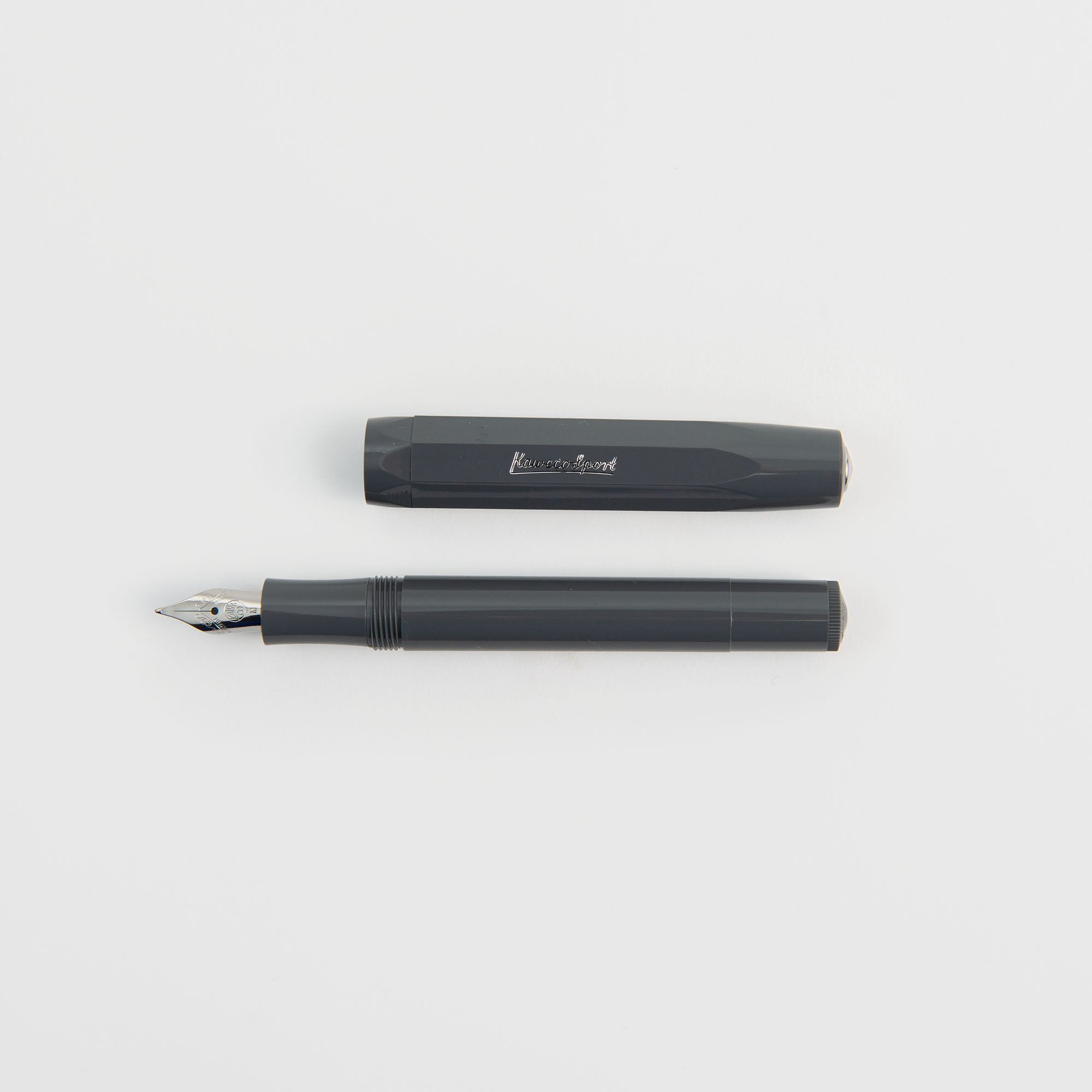 Ein Kaweco Classic Sport - Füllhalter von Kaweco in Dunkelgrau mit Goldfeder ist ohne Kappe abgebildet und liegt parallel zu seiner passenden Kappe auf einem schlichten weißen Hintergrund.