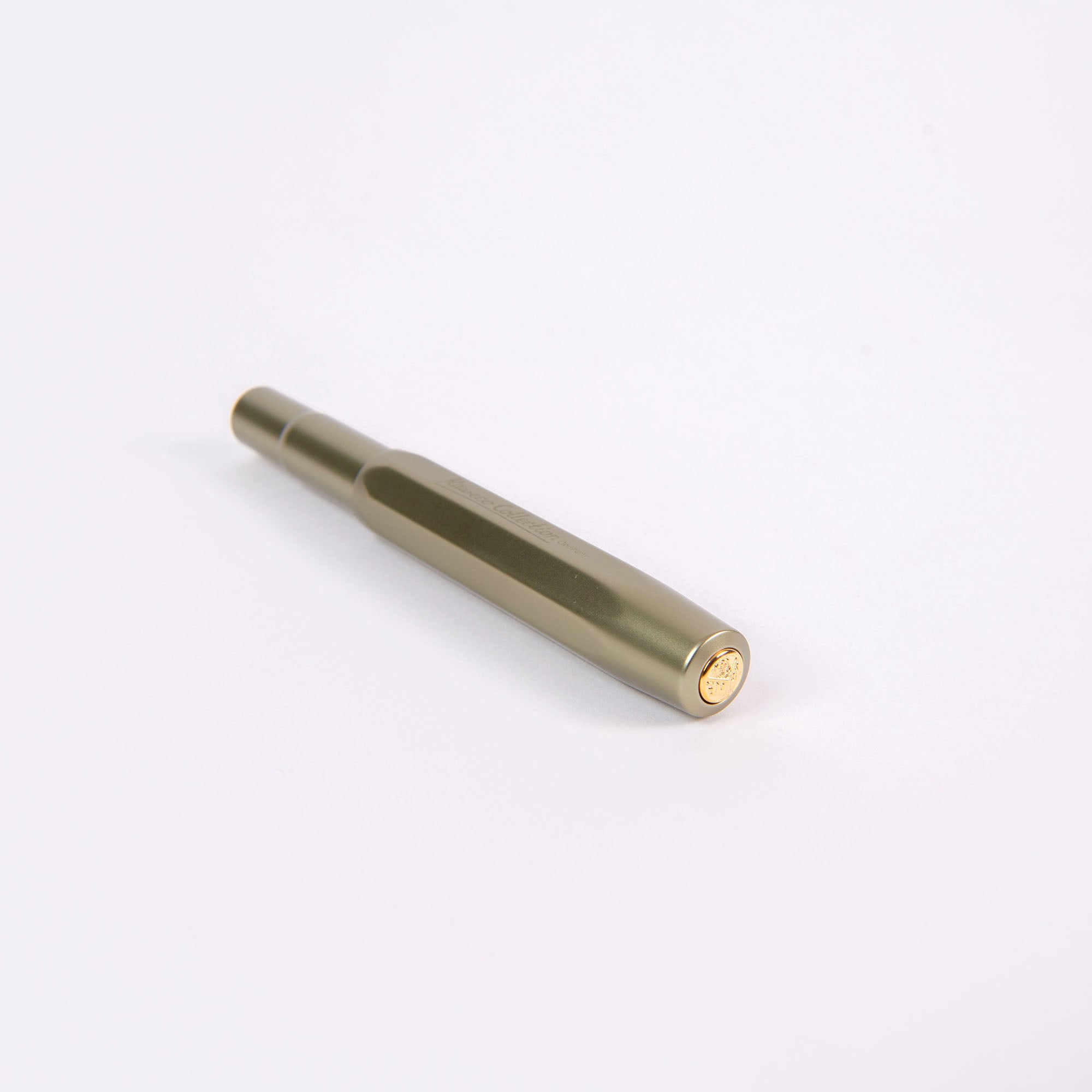 Ein schlanker, limitierter Olivine Kaweco Füllhalter mit sechseckigem Körper ruht auf einer weißen Oberfläche, mit spitzer Spitze und goldenem Emblem. Sein minimalistisches Aluminiumdesign bietet eine moderne Ästhetik, perfekt als Taschenfüllhalter.