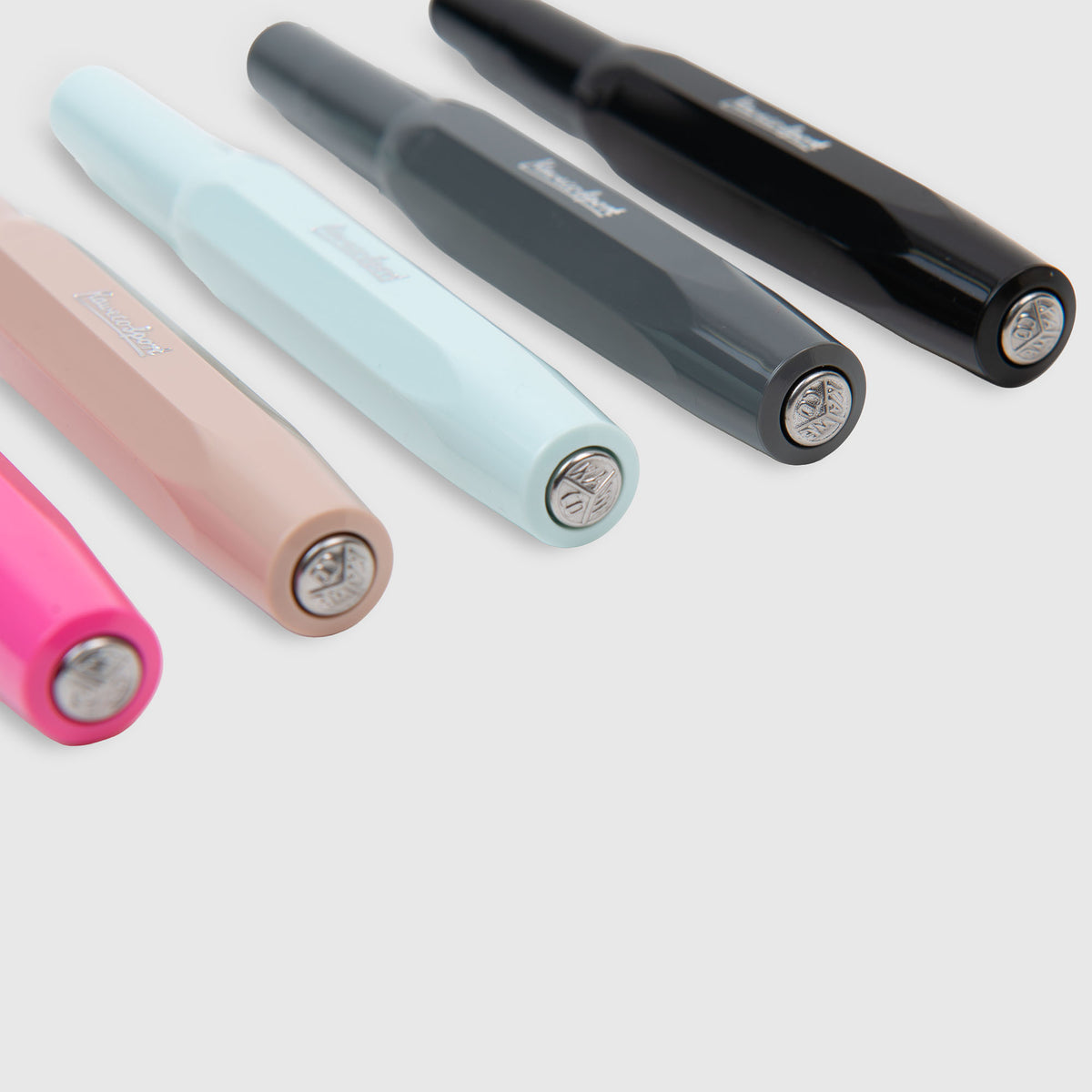 Fünf Kaweco Skyline Sport – Füllhalter in den Farben Rosa, Hellrosa, Hellblau, Schwarz und Dunkelgrau sind diagonal auf einer weißen Fläche angeordnet. Ihre Kappen sind nach vorne gerichtet, um die Kaweco-Markenlogos zu präsentieren und den unverwechselbaren Stil jedes einzelnen Füllhalters hervorzuheben.