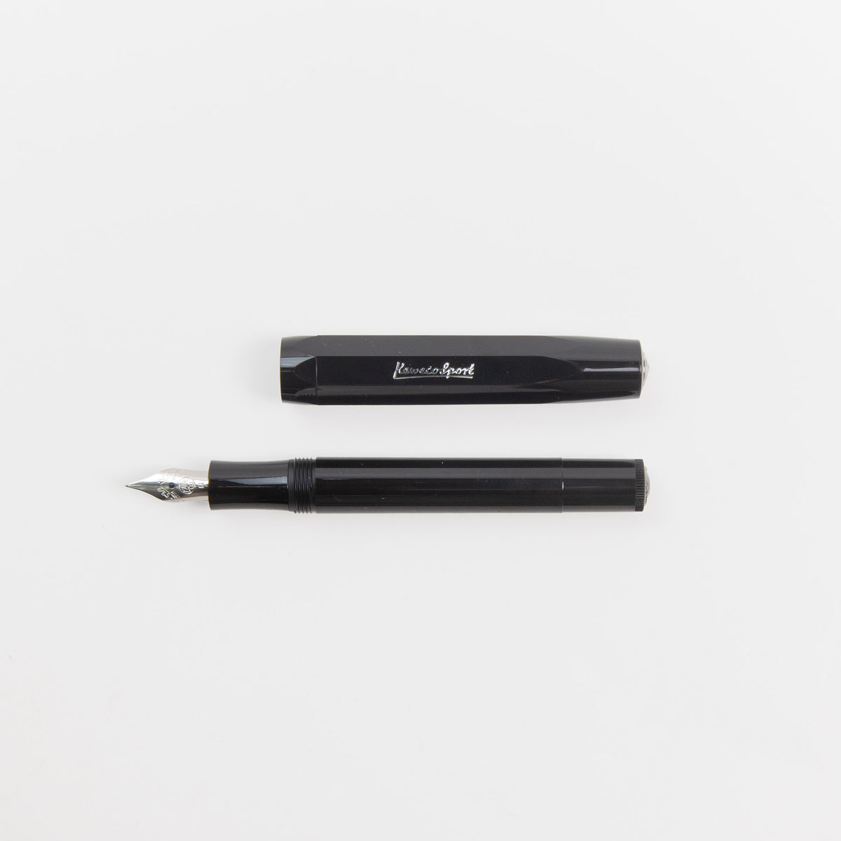 Ein schwarzer Kaweco Skyline Sport – Füllhalter von Kaweco, ohne Kappe, wobei die Kappe auf dem Stift aufliegt, ruht auf einer weißen Oberfläche. Die silberne Feder glänzt, während die Beschriftung auf der Kappe die zeitlose Eleganz dieses klassischen Schreibgeräts unterstreicht.