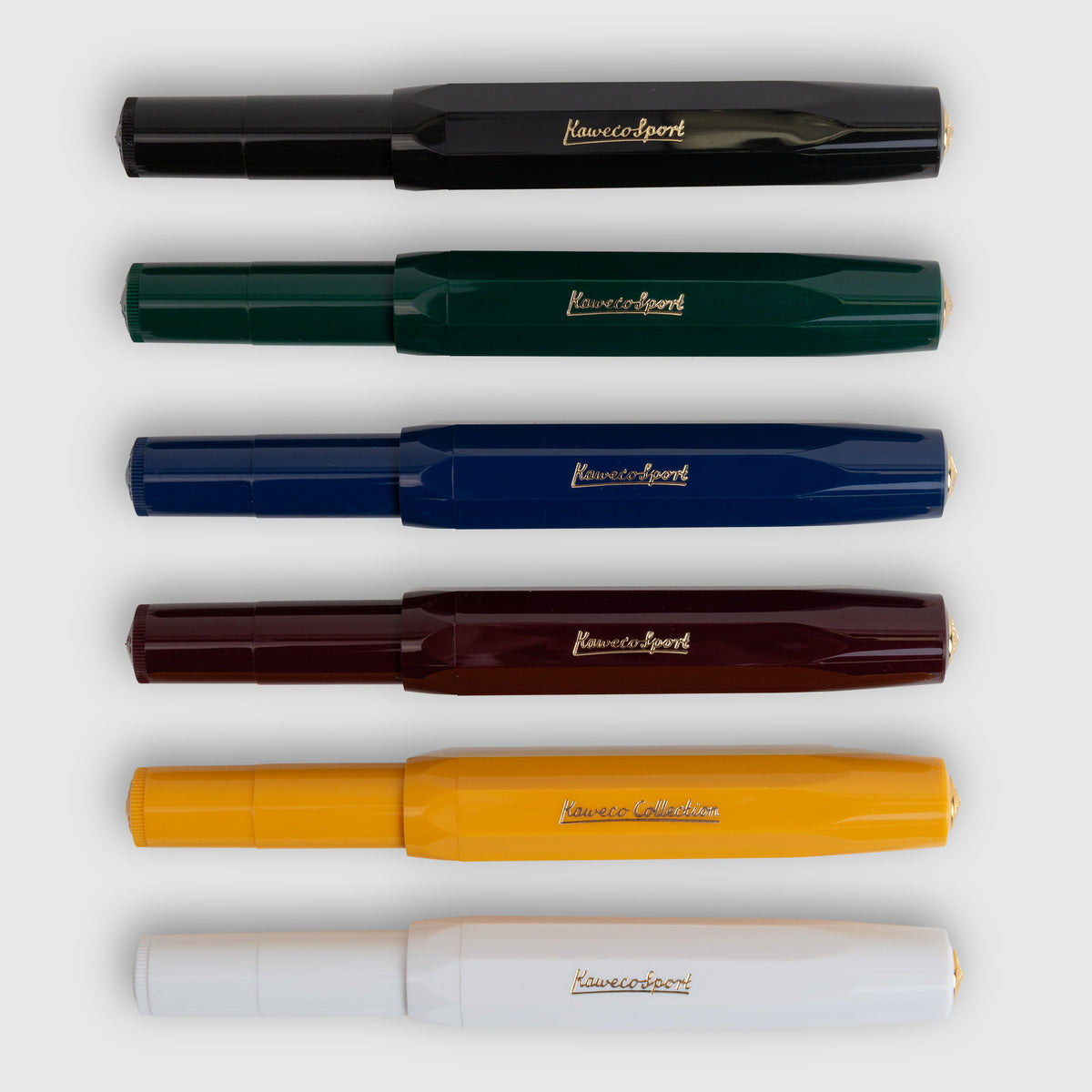 Sechs Kaweco Classic Sport – Füllhalter von Kaweco sind horizontal in den Farben Schwarz, Grün, Blau, Burgunderrot, Gelb und Weiß auf hellgrauem Hintergrund angeordnet. Jeder Füllhalter trägt ein goldenes oder silbernes Logo, wobei einige durch eine goldene Feder elegant akzentuiert sind.