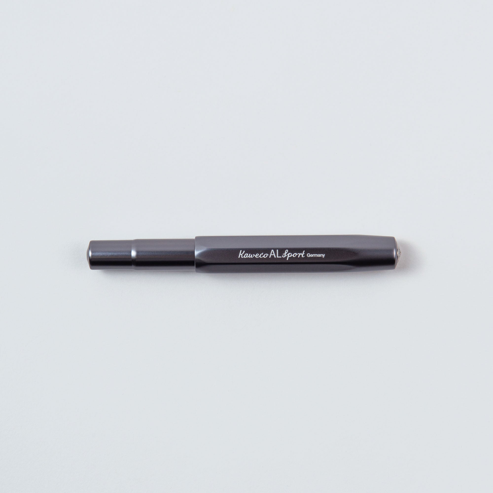 Ein schwarzer „Kaweco“ Füllhalter M – Aluminium, mit der Gravur „Germany“ auf dem Gehäuse, ruht elegant auf einer hellgrauen Oberfläche.