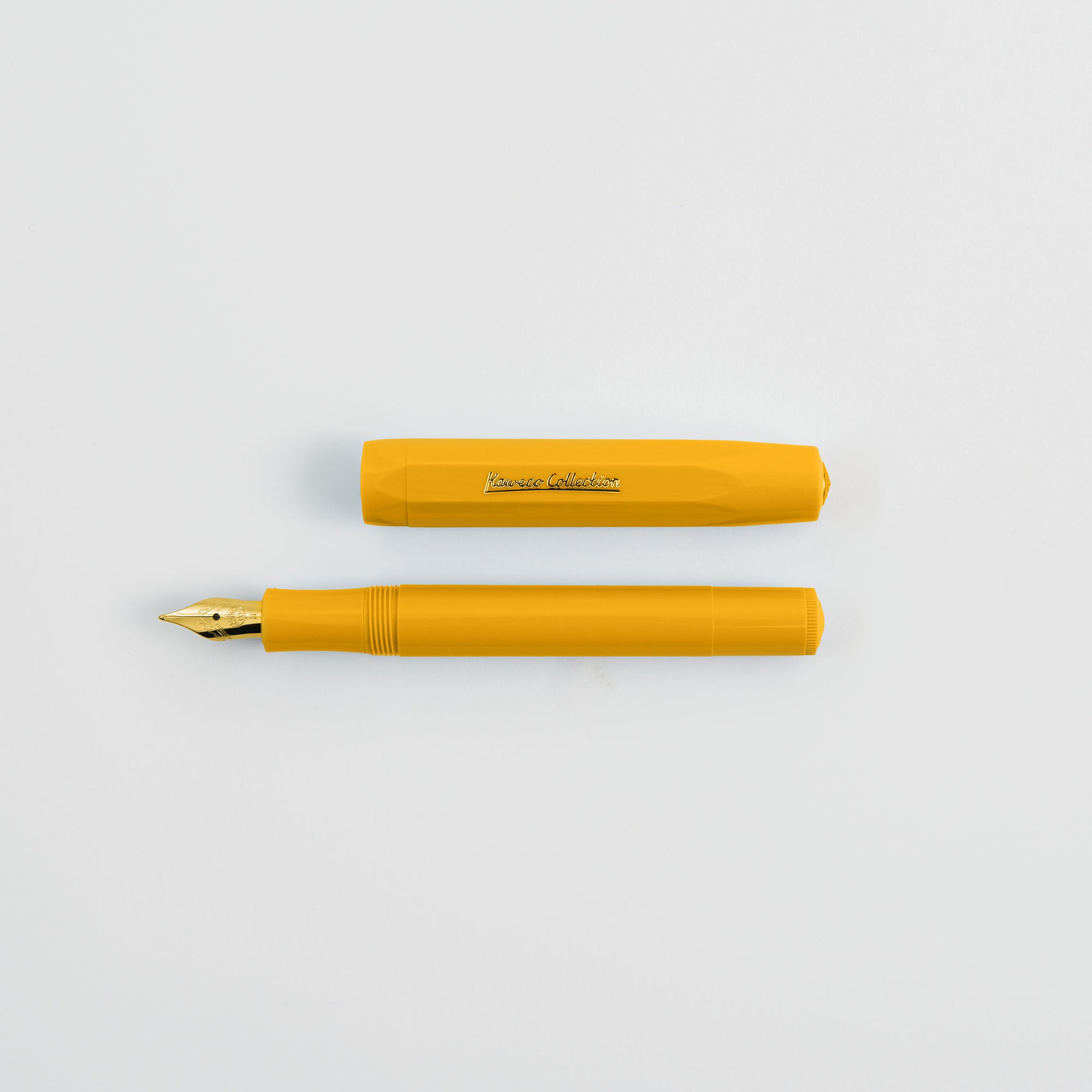 Ein gelber Kaweco Classic Sport - Füllhalter von Kaweco liegt mit abgenommener Kappe auf einer weißen Fläche und ist oberhalb des Stiftes platziert. Der Stift hat eine goldene Feder, während die Kappe einen Text zeigt.