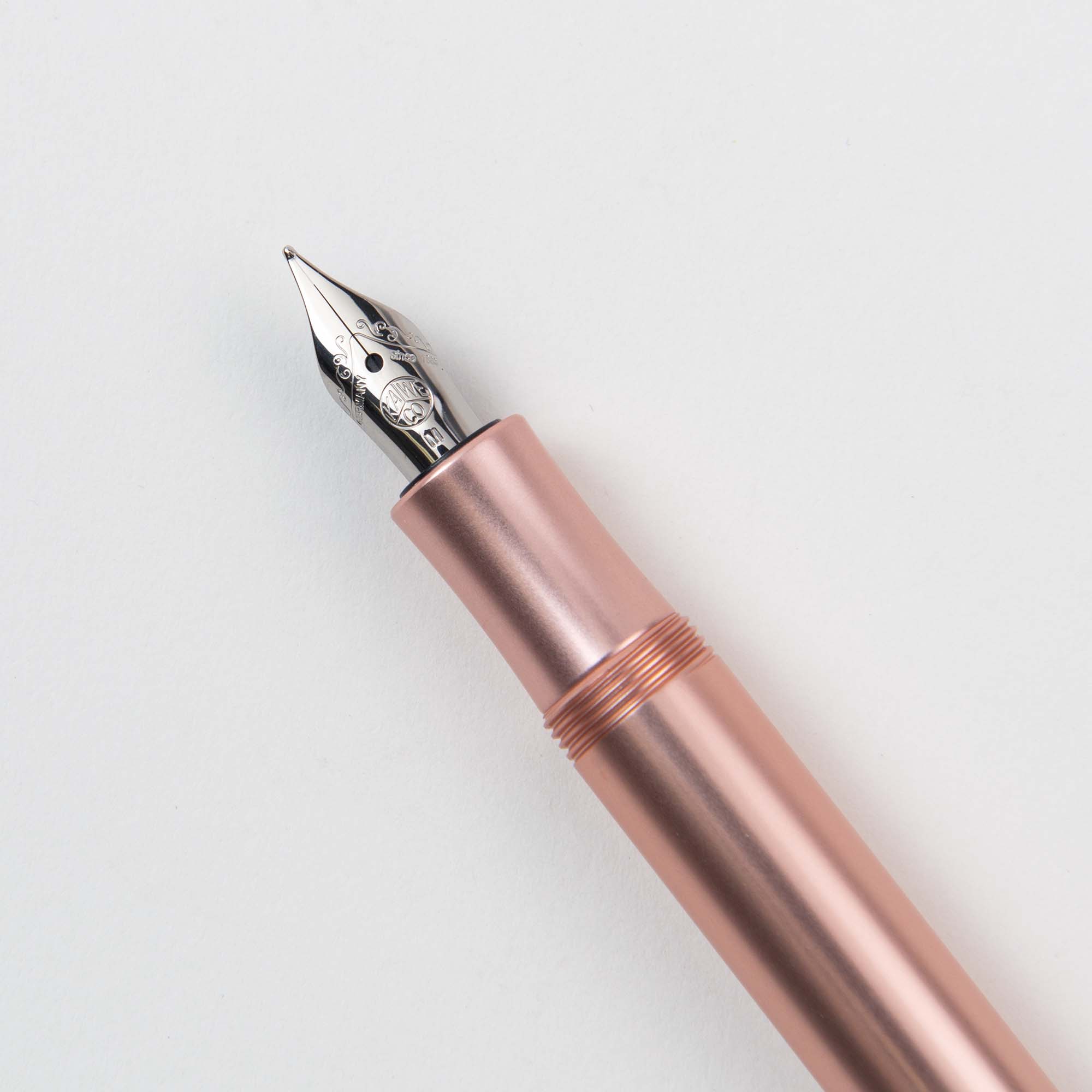 Eine Nahaufnahme des Kaweco Füllhalters M – Aluminium zeigt seinen metallischen Roségoldkörper und die silberne Feder vor einem schlichten weißen Hintergrund und strahlt eine Eleganz aus, die an einen klassischen Kugelschreiber erinnert.