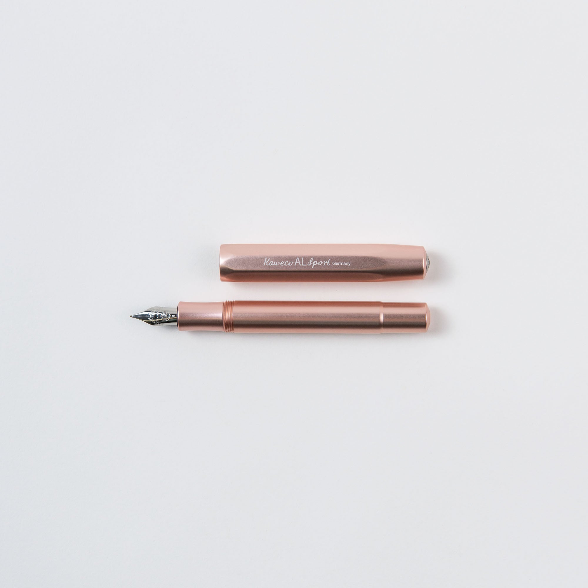 Ein roségoldener Kaweco Füllhalter M Füllfederhalter ruht auf weißem Untergrund. Der Stift verfügt über eine silberne Feder und ein Aluminiumgehäuse, während die Kappe mit der Gravur „Kaweco AL Sport Germany“ die Eleganz der Kompaktgröße unterstreicht.