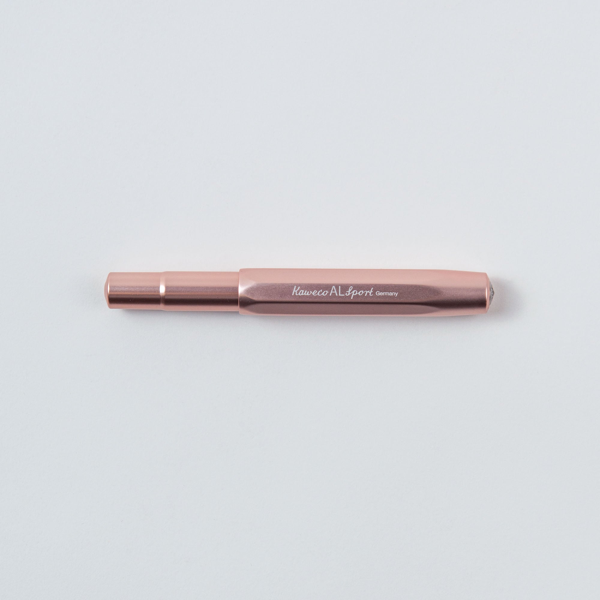 Ein roségoldener Stift der Marke „Kaweco“ mit der Gravur „AL Sport Germany“ ruht wunderschön auf einem hellgrauen Hintergrund und unterstreicht seine kompakte Größe und sein zeitloses Design.