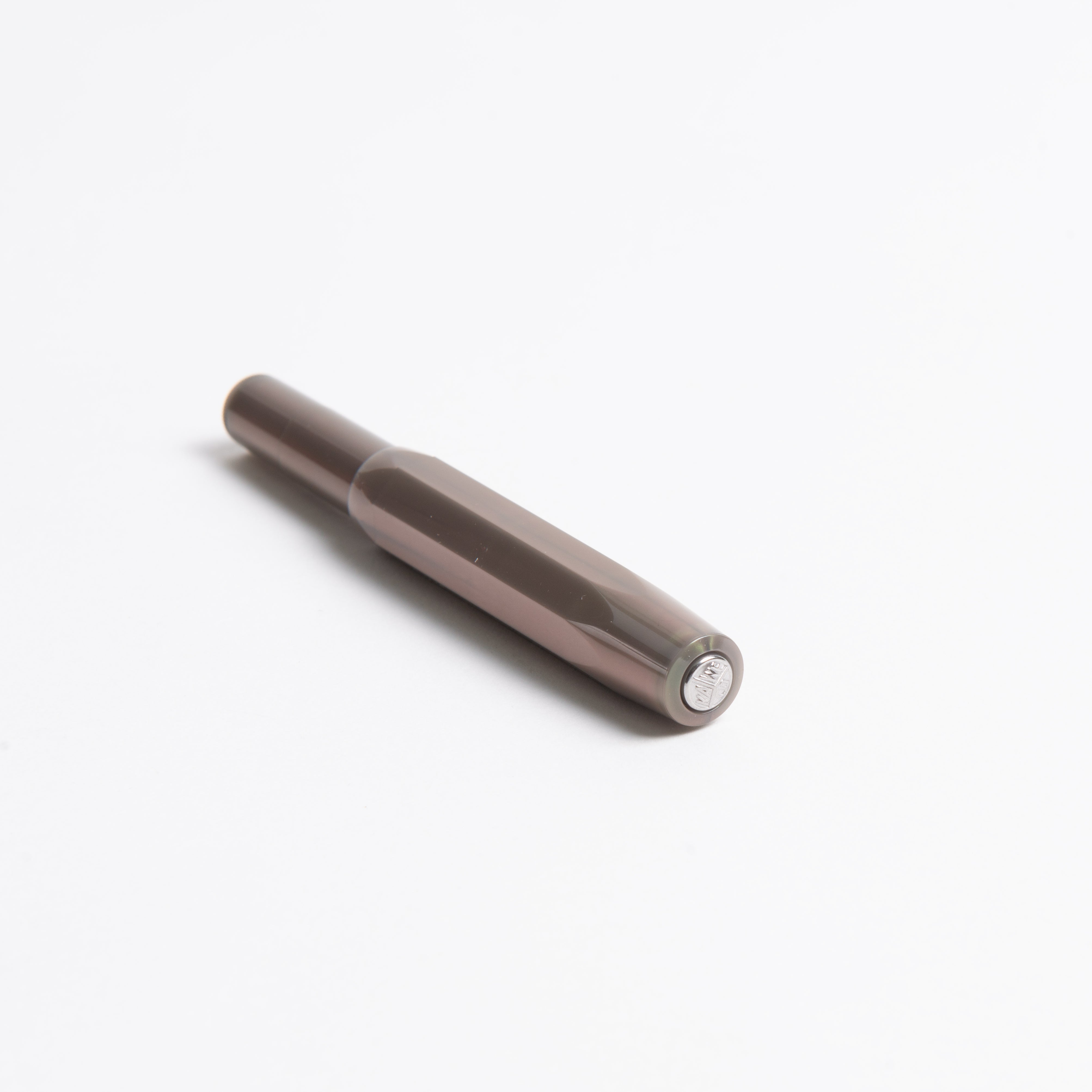 Ein Kaweco Lunar Sport - Füllhalter von Kaweco, dunkelbraun-metallic mit glänzendem ABS-Kunststoff-Finish, liegt diagonal auf weißem Grund. Der Füllhalter mit Kappe hat ein kleines rundes Emblem am Ende.