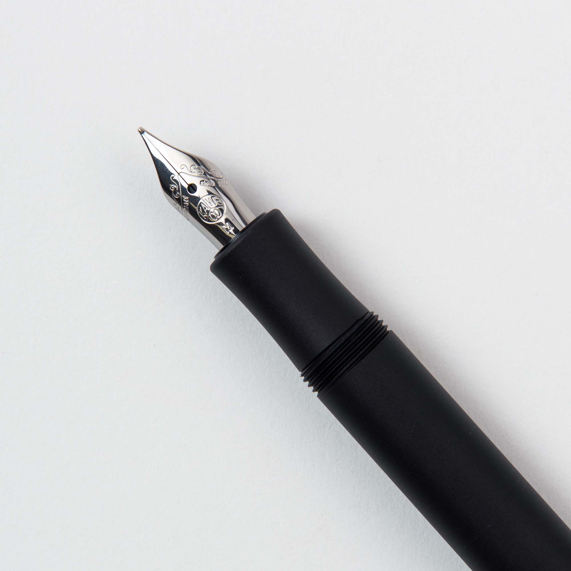 Eine Nahaufnahme des Kaweco Füllhalters M – Aluminium, eines schwarzen Füllfederhalters mit einer silbernen Feder mit komplizierten Mustern, ähnlich einem echten Klassiker, der anmutig auf einer weißen Oberfläche ruht.