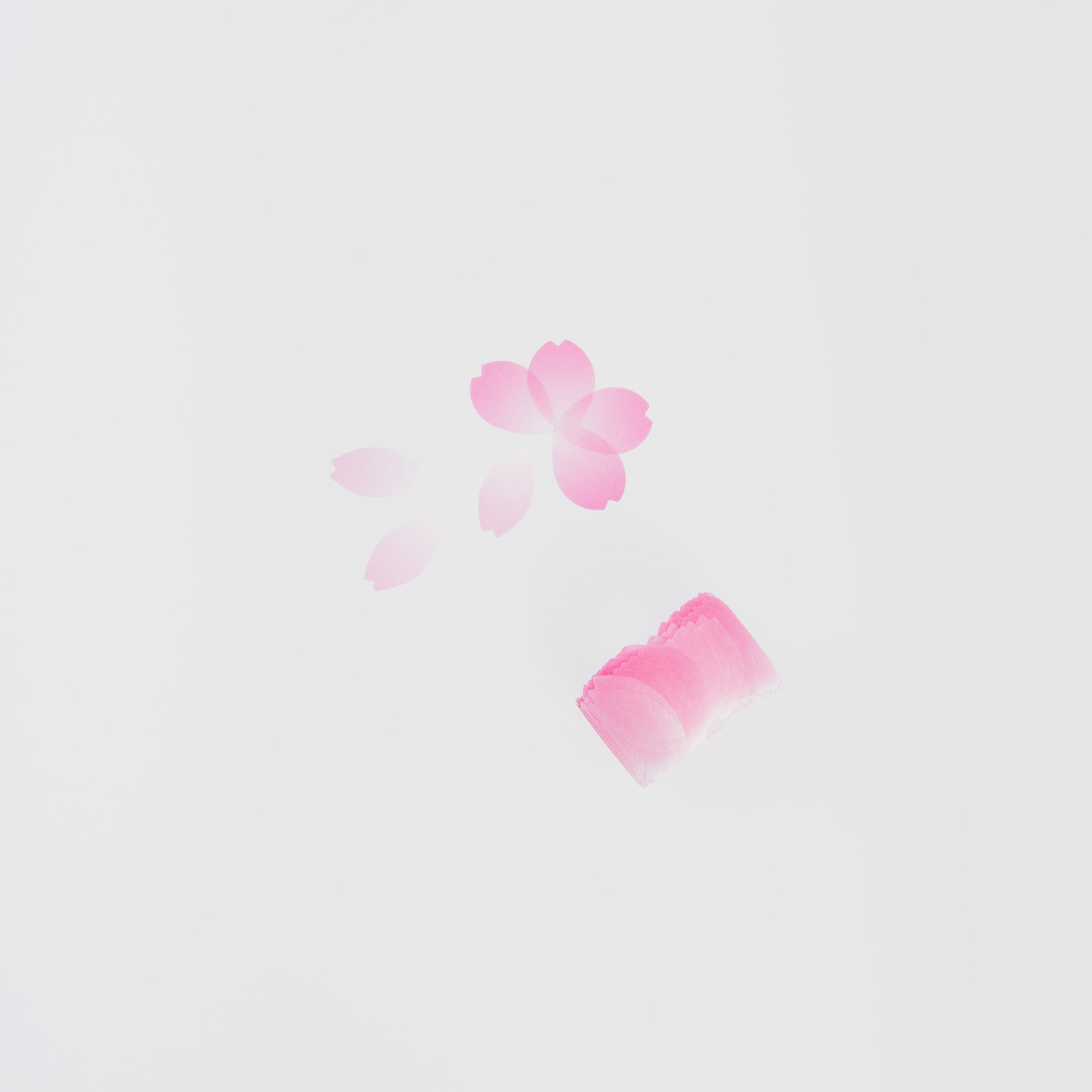 Ein rosa Stempel mit Kirschblütenmotiv liegt auf einer weißen Oberfläche und hinterlässt Abdrücke von Kirschblüten und Blütenblättern, die daneben verstreut sind, wodurch ein künstlerischer Effekt entsteht, der dem Washi Tape „Kirschblüte“ von Paper Poetry ähnelt.