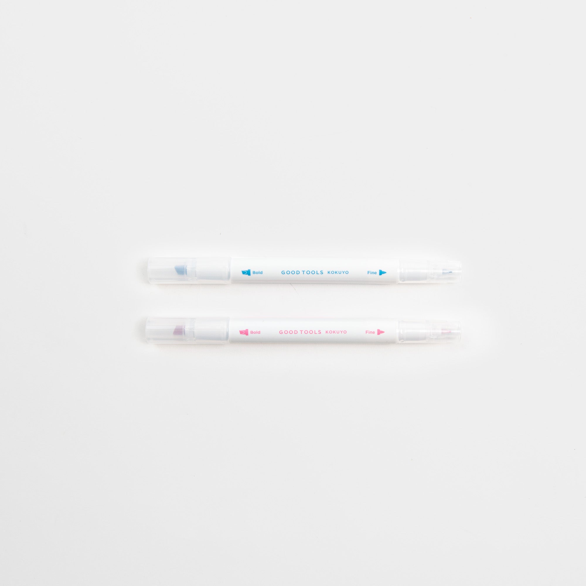 Zwei Kokuyo Two-Way Marking Pens mit klaren Kappen sind parallel auf einem weißen Hintergrund platziert. Der obere Stift hat die blaue Aufschrift "GOOD TOOLS", der untere ist rosa. Ideal für jede Journaling-Sammlung.
