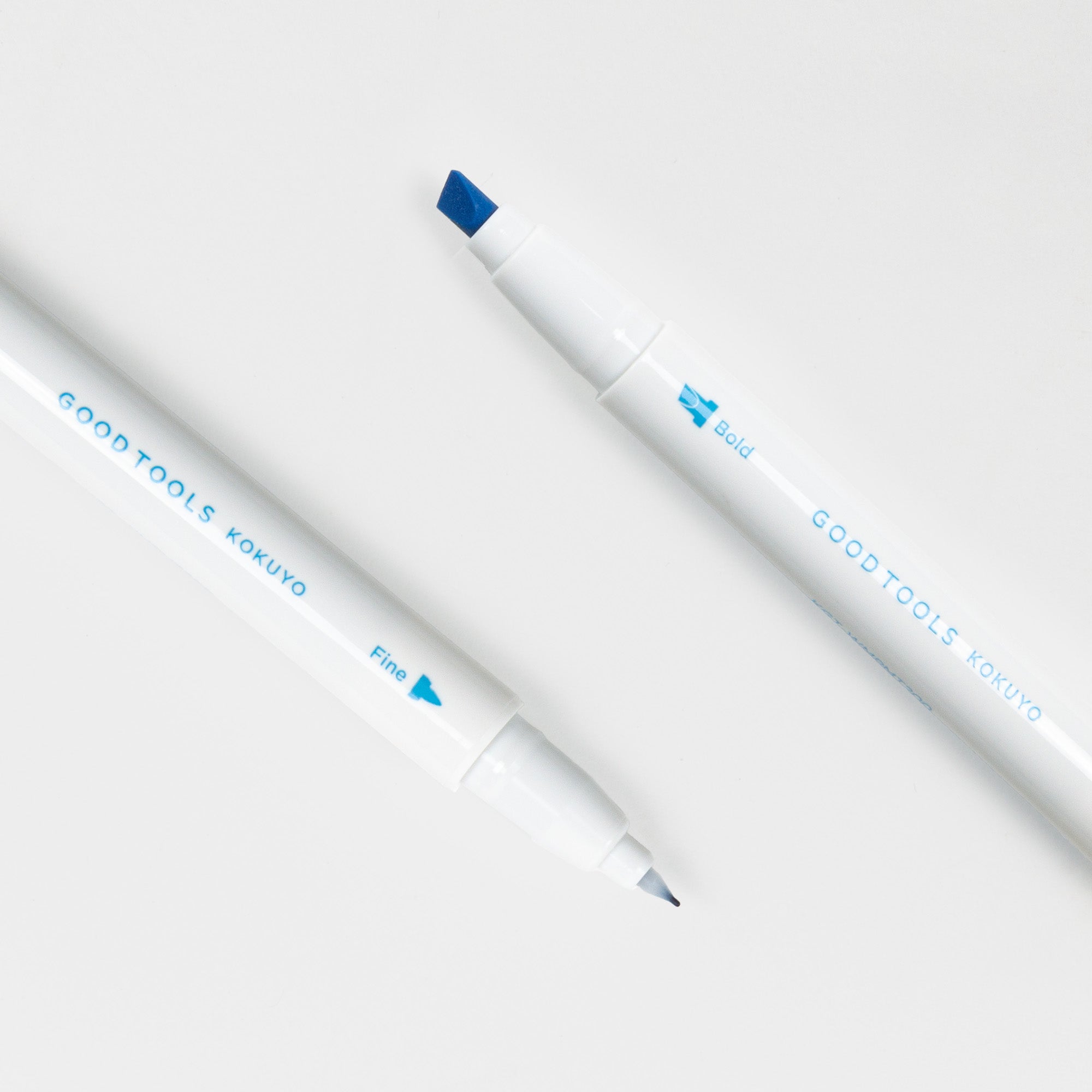 Zwei weiße Kokuyo Two-Way Marking Pens liegen auf einer weißen Oberfläche und haben jeweils eine klare blaue Schrift und zwei blaue Spitzen - fett und fein - und sind damit die ideale Ergänzung für jede Schreibsammlung.