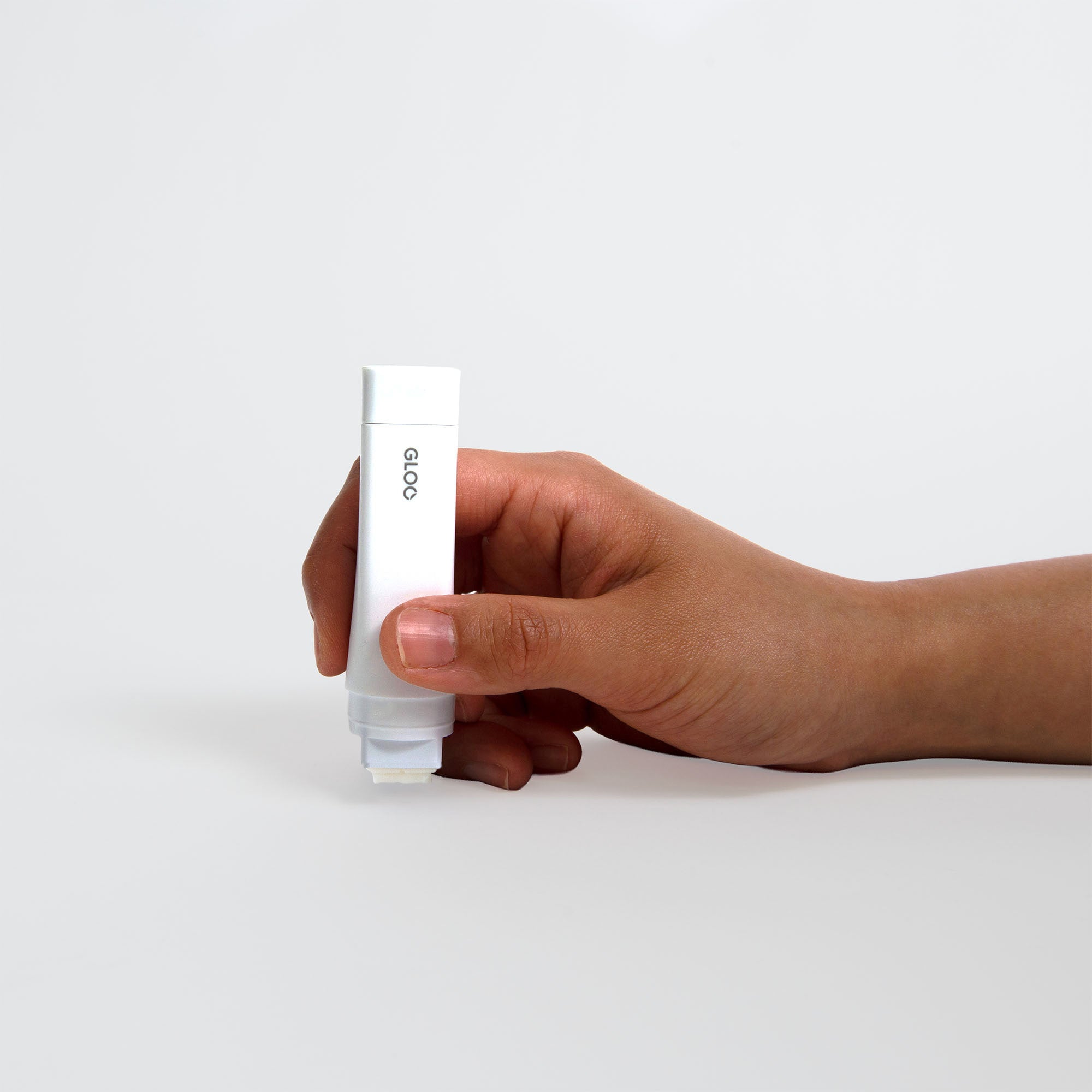 Eine Hand hält eine weiße rechteckige Tube mit der Aufschrift Kokuyo Gloo Klebestift - Permanent von Kokuyo, inspiriert von Nendo Design, vor einem schlichten weißen Hintergrund.
