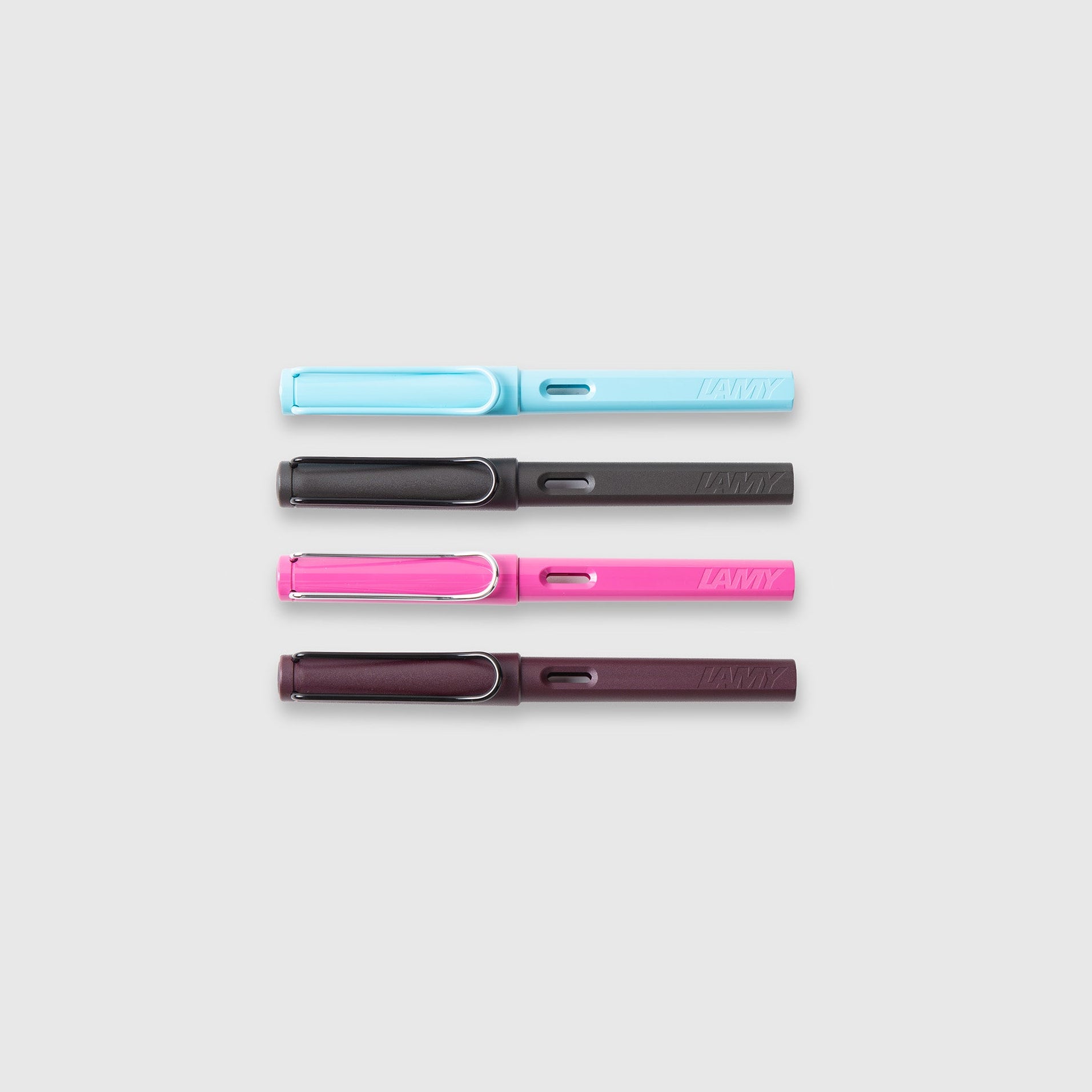 Vier LAMY safari Füllhalter von Lamy in pastellblau, dunkelgrau, hellrosa und dunkelviolett ASA-Kunststoff sind waagerecht auf einem hellgrauen Hintergrund angeordnet.