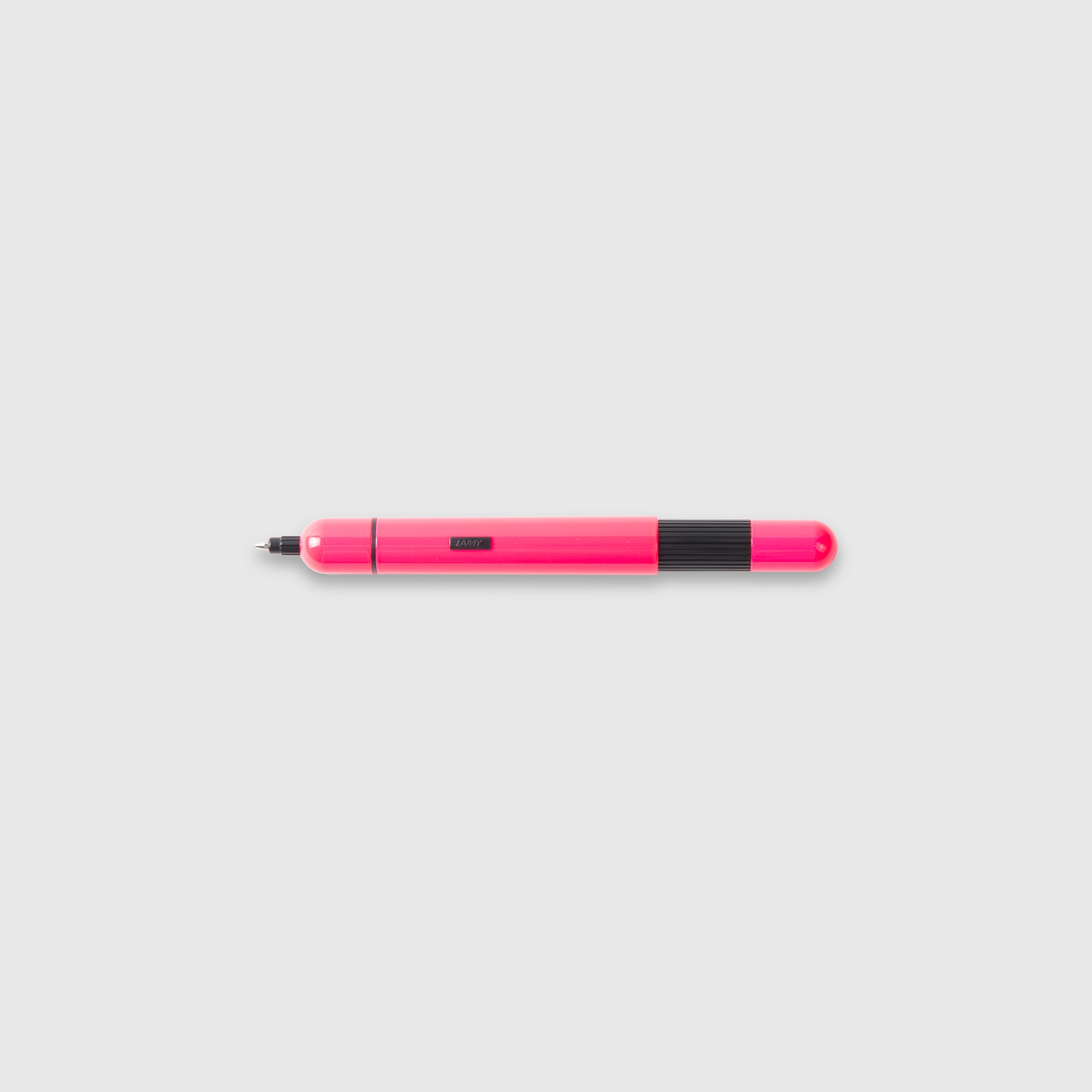 Ein leuchtend pinker LAMY pico Kugelschreiber von Lamy mit schwarzem Griffstück und feiner Spitze liegt waagerecht auf einem schlichten hellgrauen Hintergrund.