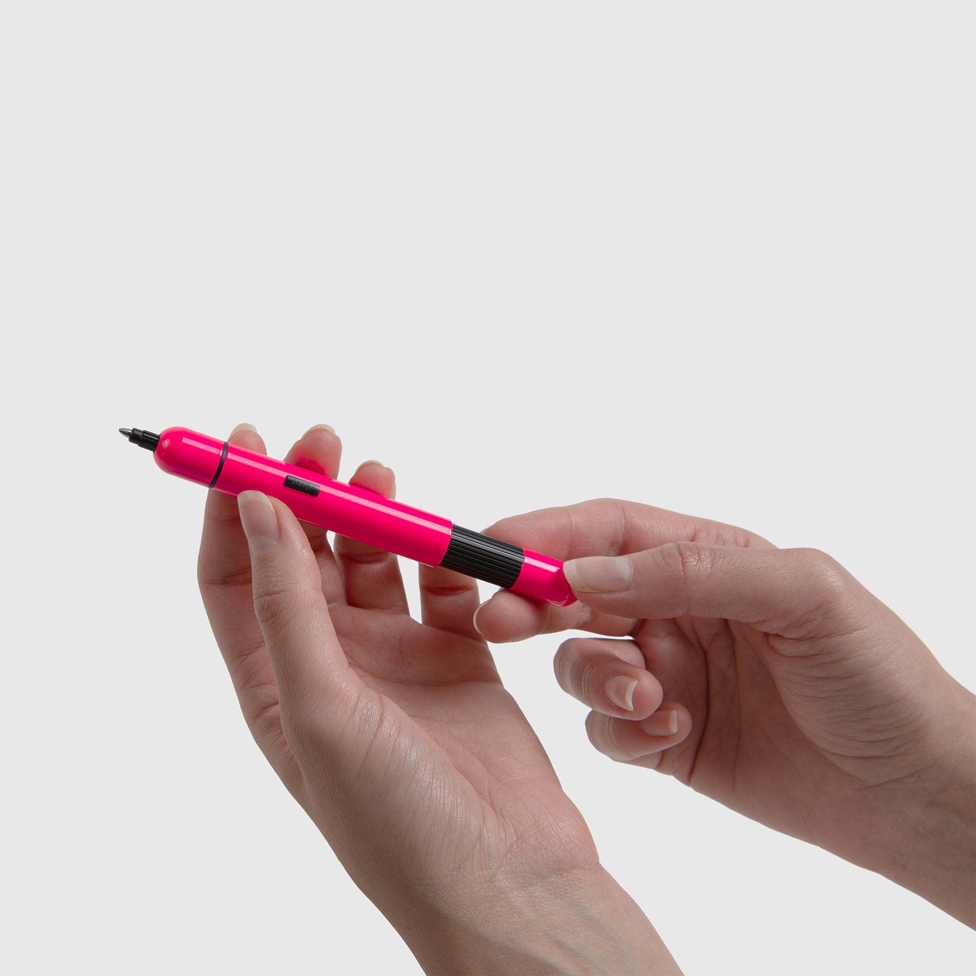 Jemand hält einen leuchtend rosa-schwarzen LAMY pico Kugelschreiber von Lamy in den Händen mit einem schlichten, hellgrauen Hintergrund.