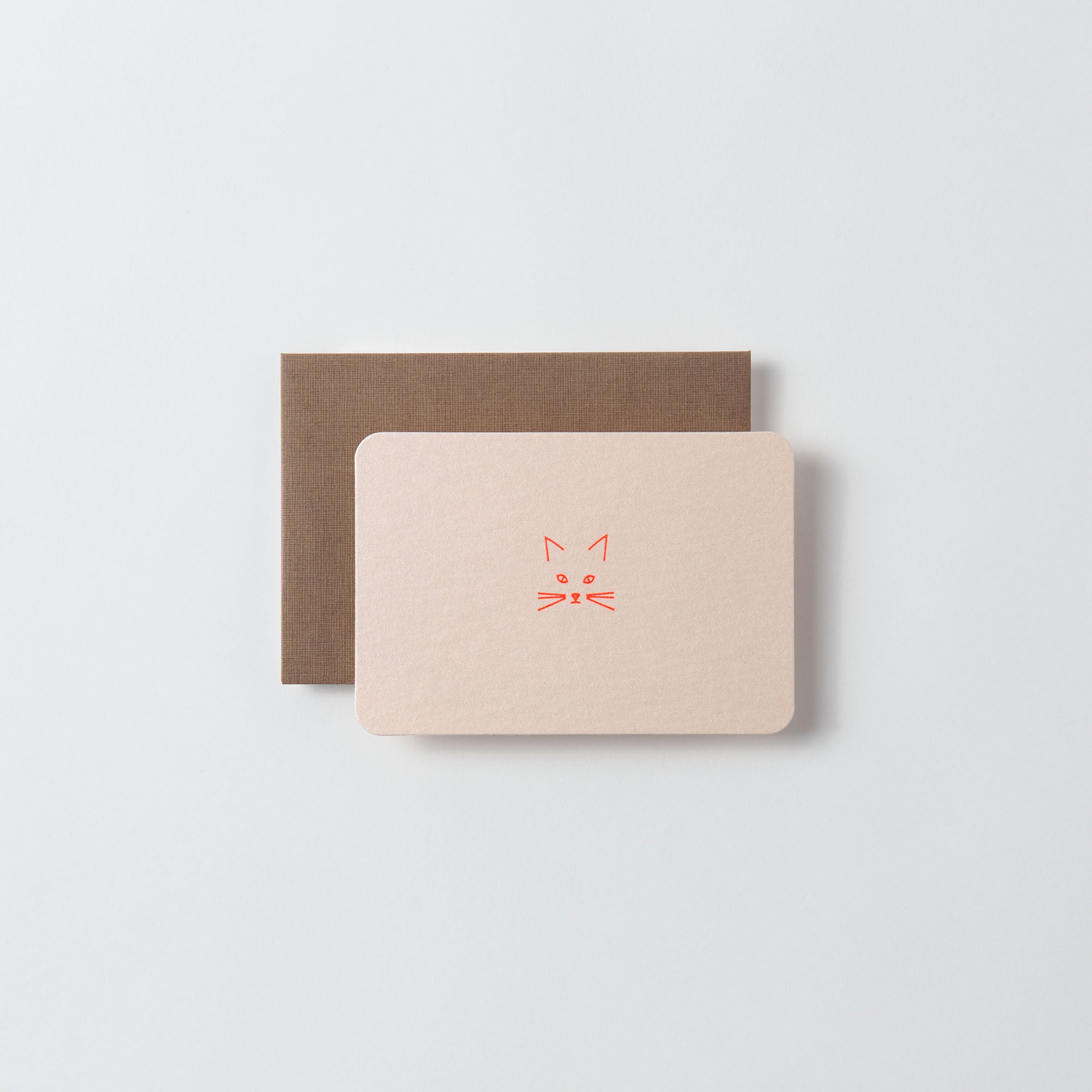 Zwei rechteckige Karten auf hellem Hintergrund. Die obere Karte ist die Miau - Mini Karte von Le Typographe in Beige mit einem orangefarbenen, minimalistischen Katzengesicht. Die untere Karte ist dunkelbraun und teilweise sichtbar.