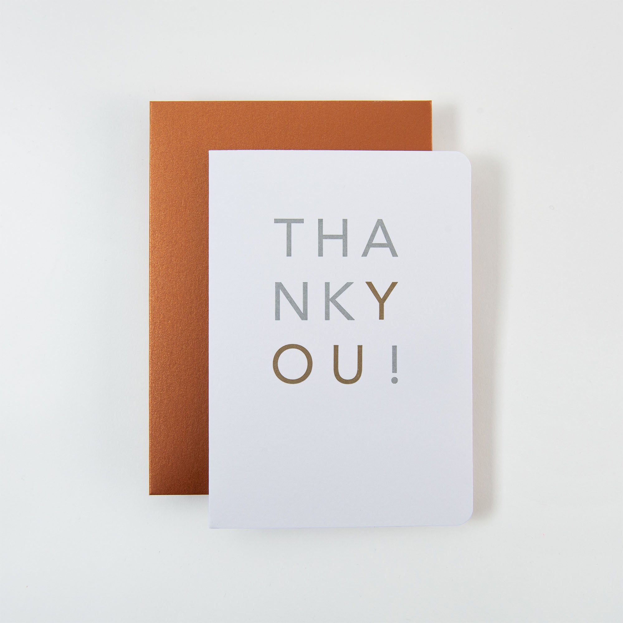 Eine Le Typographe THANKYOU Karte und Kuvert zeigt „DANKE!“ in kräftigem Grau und Gold auf einem geschlossenen orangefarbenen Umschlag, elegant vor einem weißen Hintergrund.