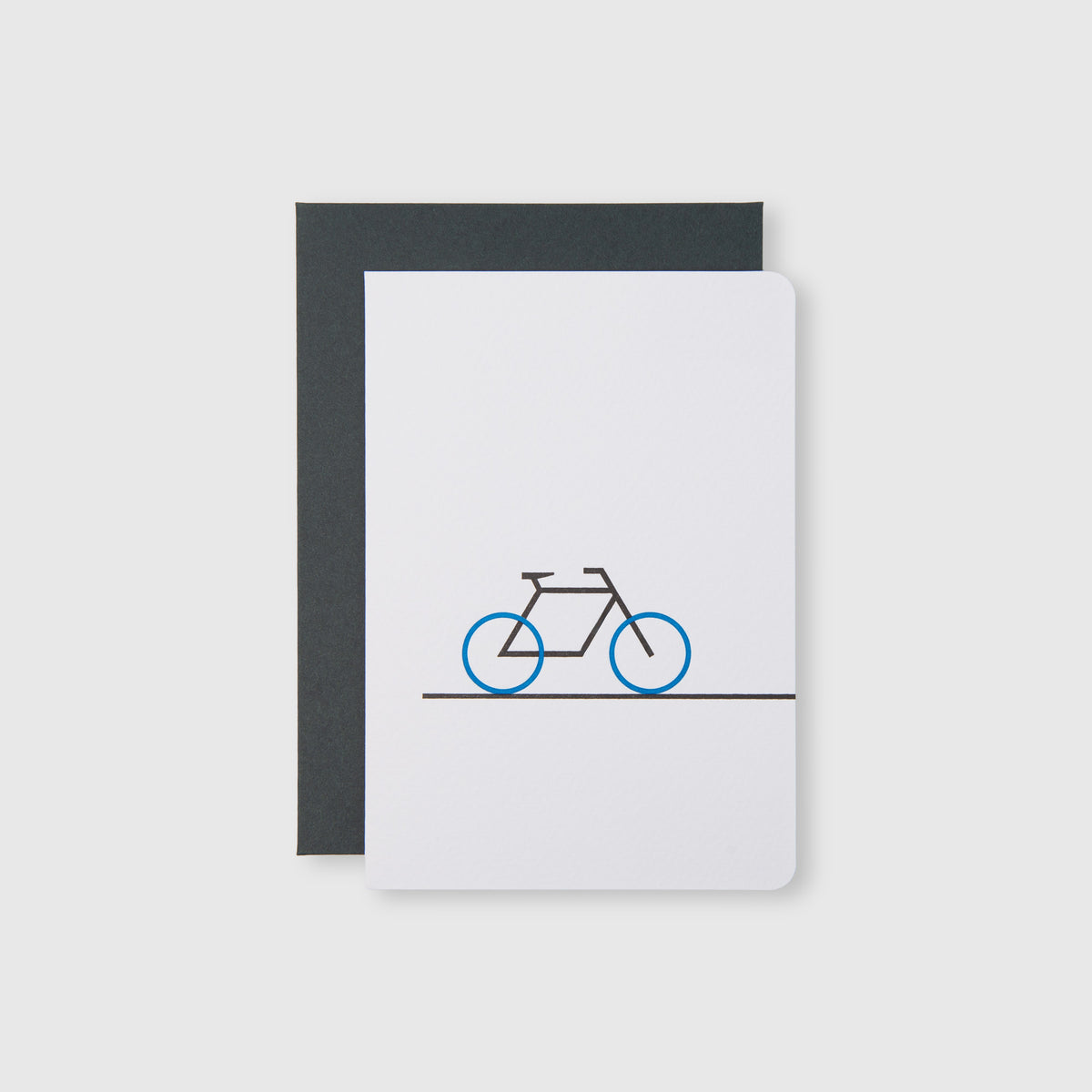 Klappkarte Fahrrad – Weiße Klappkarte von Le Typographe mit einer minimalistischen Fahrradillustration mit blauen Rädern, präsentiert in einem dunklen Umschlag.