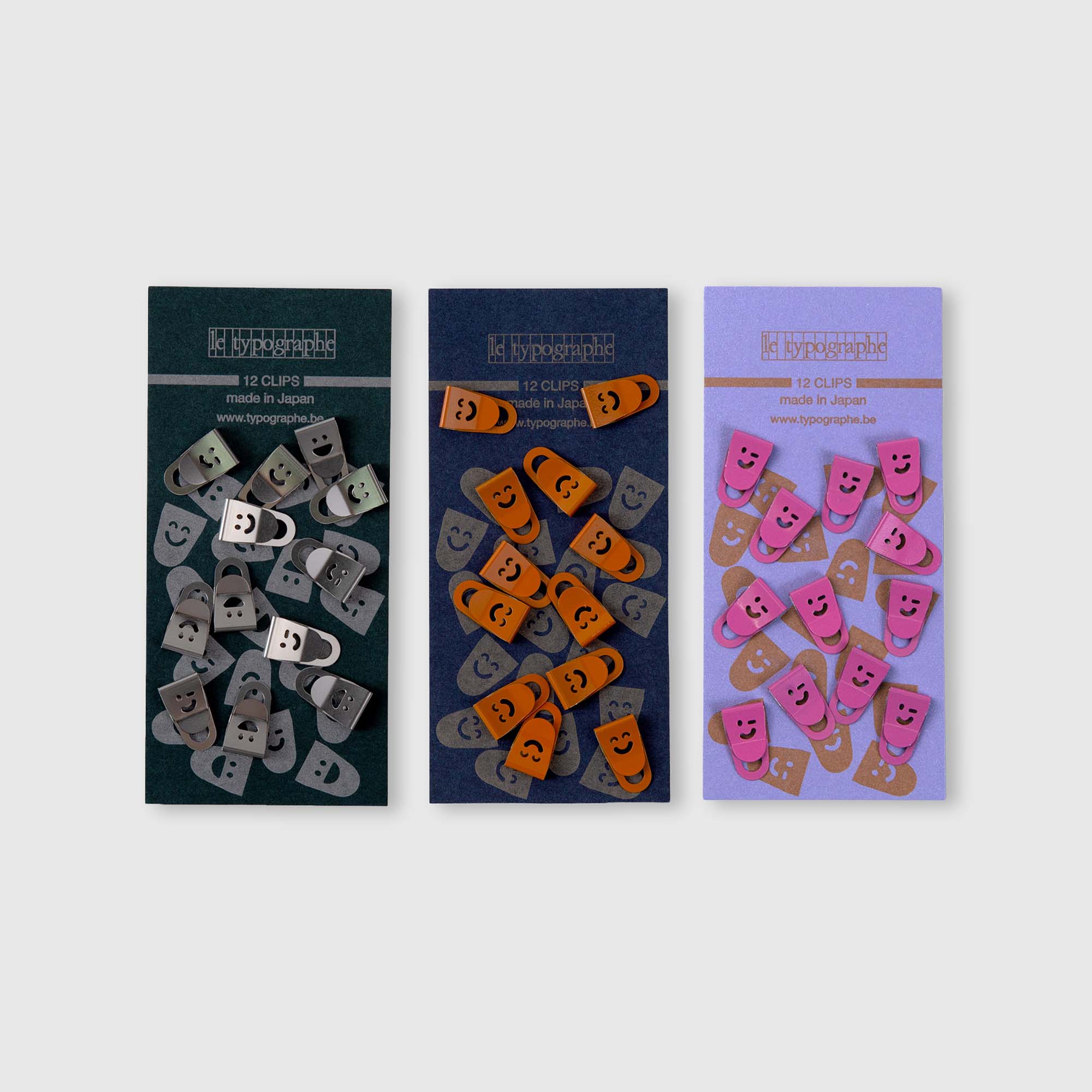 Drei Packungen mit 12 Mini Clips Smiley von Le Typographe, perfekt für die Schreibtischorganisation. Jedes Set besteht aus silbernen, orangefarbenen und rosafarbenen Metallclips mit beschrifteten Aufsätzen auf bunten Hintergründen.