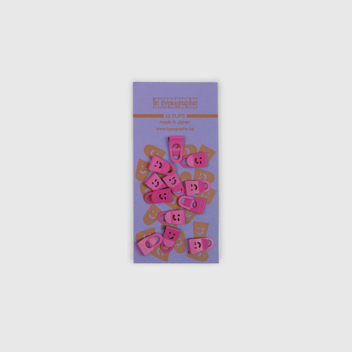 Zwölf rosa Mini-Clips aus Metall mit Smiley-Ausschnitten, angeordnet auf einem violetten Kartonträger zur Organisation auf dem Schreibtisch.
