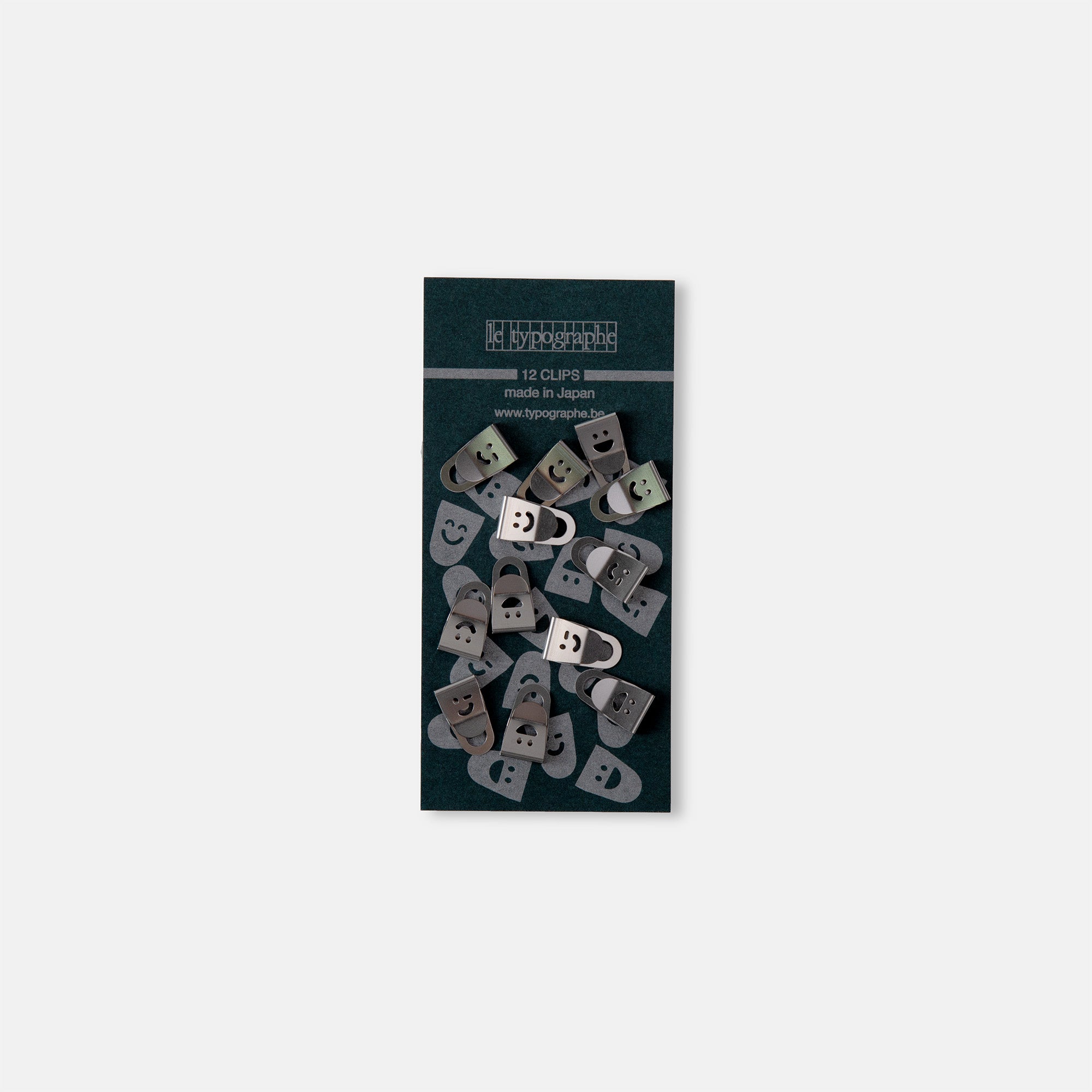 Eine 12er-Packung Le Typographe Mini Clips Smiley enthält Büroklammern aus Metall mit einem ausgeschnittenen Smiley-Motiv. Die dunkelgrüne Verpackung mit weißem Text bringt einen verspielten Touch in Ihre Schreibtischorganisation.