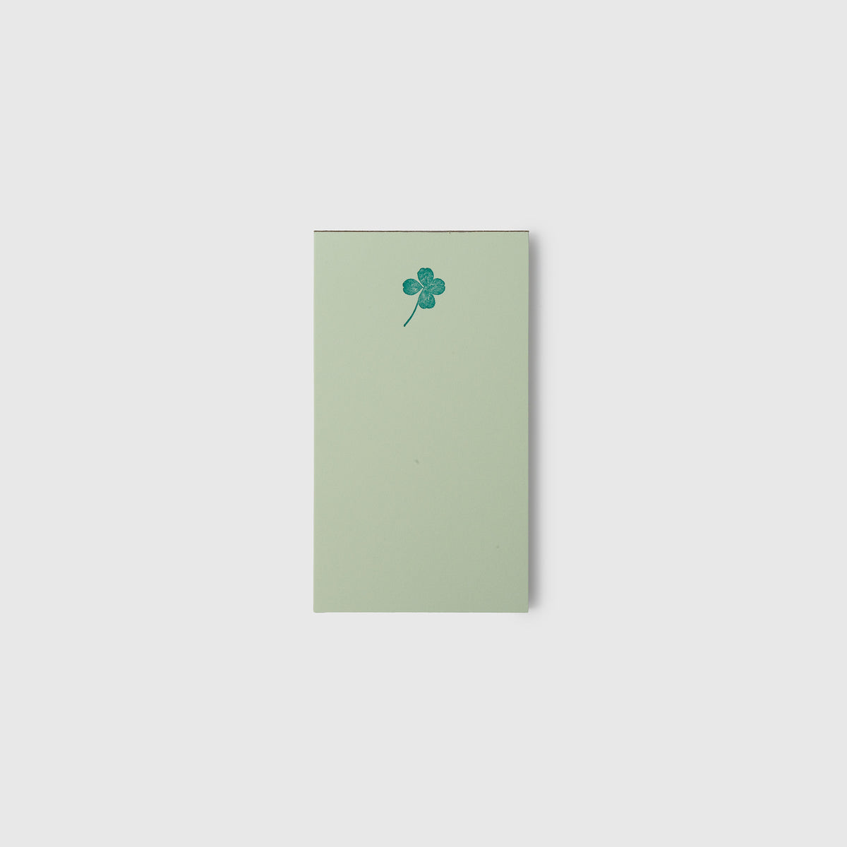 Ein rechteckiges, hellgrünes Mini-Notizbuch – Kiss Kiss, Love Love – mit einem kleinen vierblättrigen Kleeblatt, das oben aufgedruckt ist.