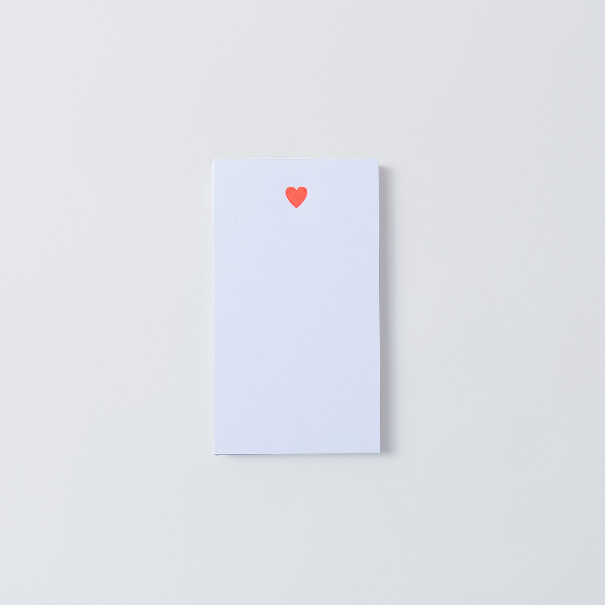 Die „Mini-Notizblöcke – Kiss Kiss, Love Love“ von Le Typographe sind weiße rechteckige Karten mit einem kleinen roten Herz oben in der Mitte, gestaltet im eleganten PapierLetterpress-Stil auf schlichtem Hintergrund.