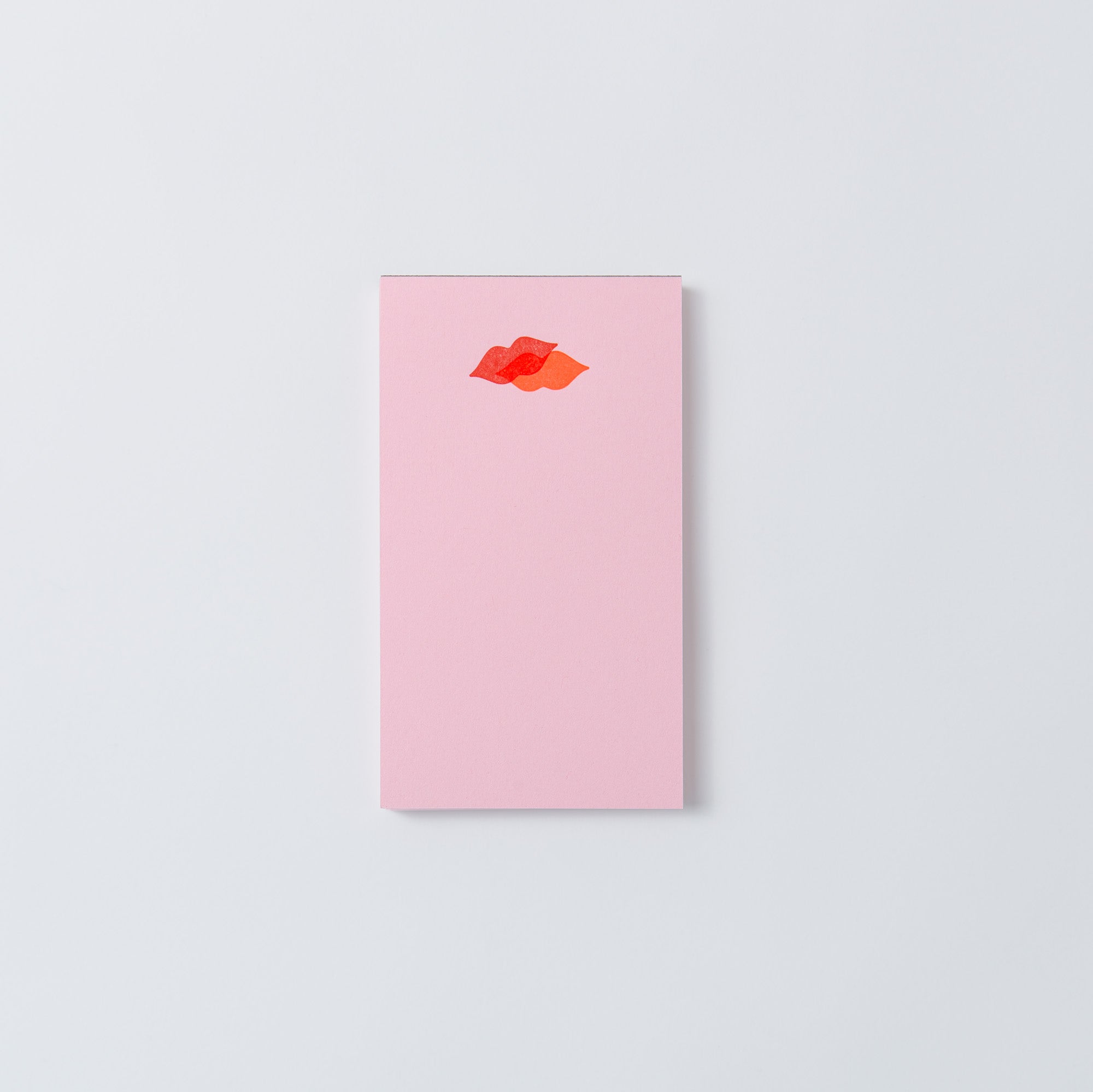Die Mini-Notizblöcke „Kiss Kiss, Love Love“ von Le Typographe haben ein rosa rechteckiges Design mit einer Illustration roter Lippen oben in der Mitte auf hellgrauem Hintergrund. Das elegante PapierLetterpress-Design verleiht jeder Seite Raffinesse.