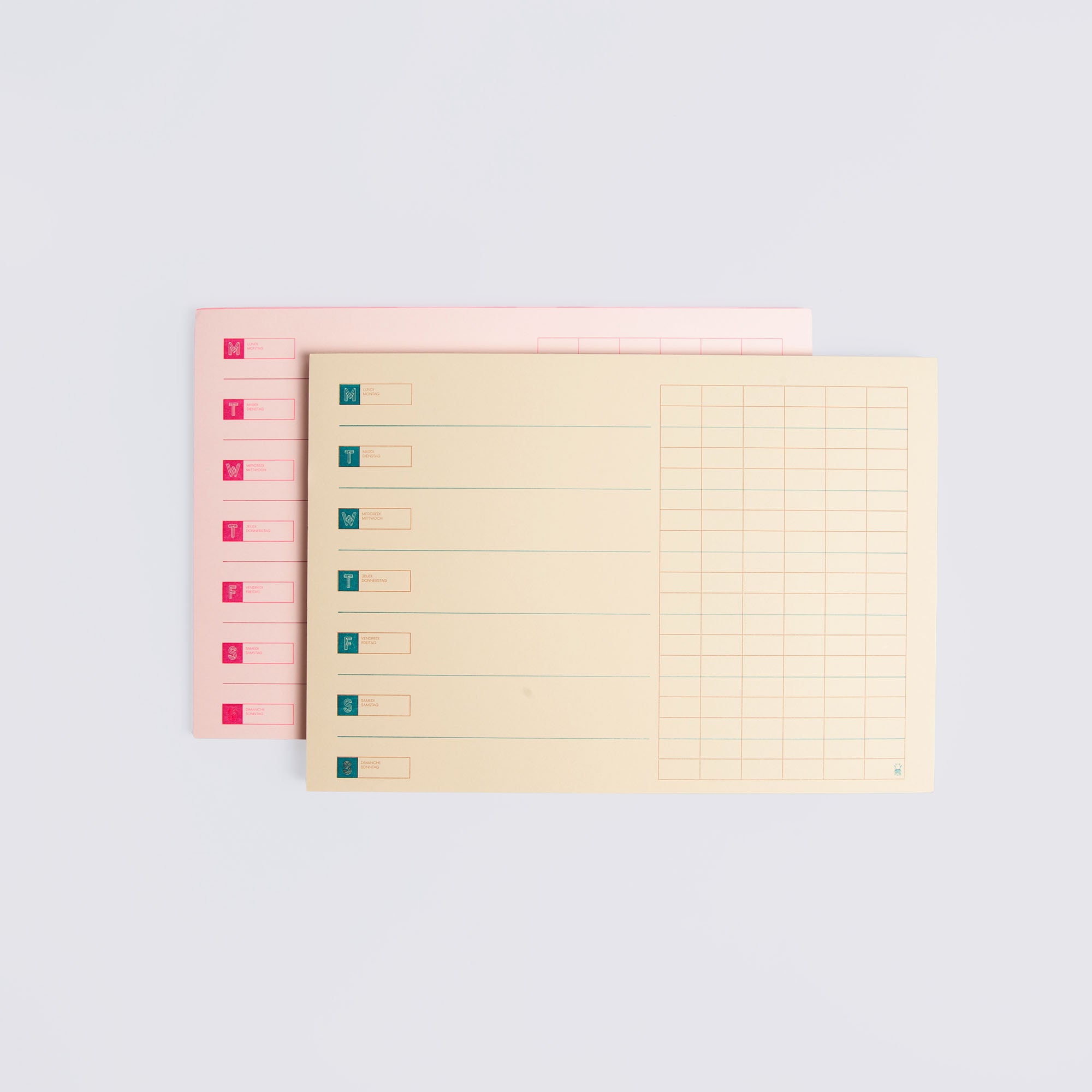 Zwei pastellfarbene rechteckige Ordner, einer pfirsichfarben und einer beige, mit farbigen Registerkarten und Rasterlinien sind versetzt gestapelt. Ideal für die Organisation Ihres Le Typographe Desk Diary Horizontal. Abgebildet auf einem schlichten weißen Hintergrund.