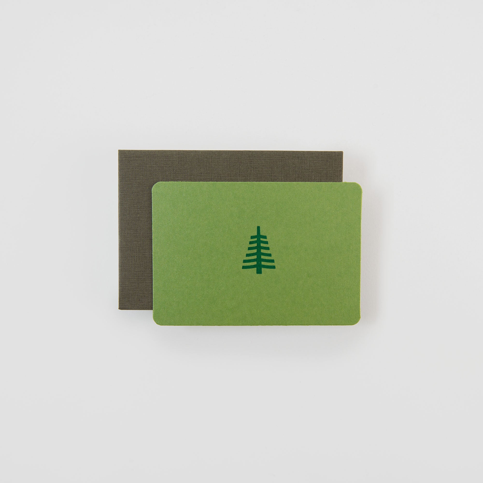 Die Tannenbaum groß - Mini Karte von Le Typographe zeigt einen schlichten dunkelgrünen Tannenbaum auf grünem Karton, der auf einem braunen Umschlag vor einem schlichten weißen Hintergrund abgebildet ist.