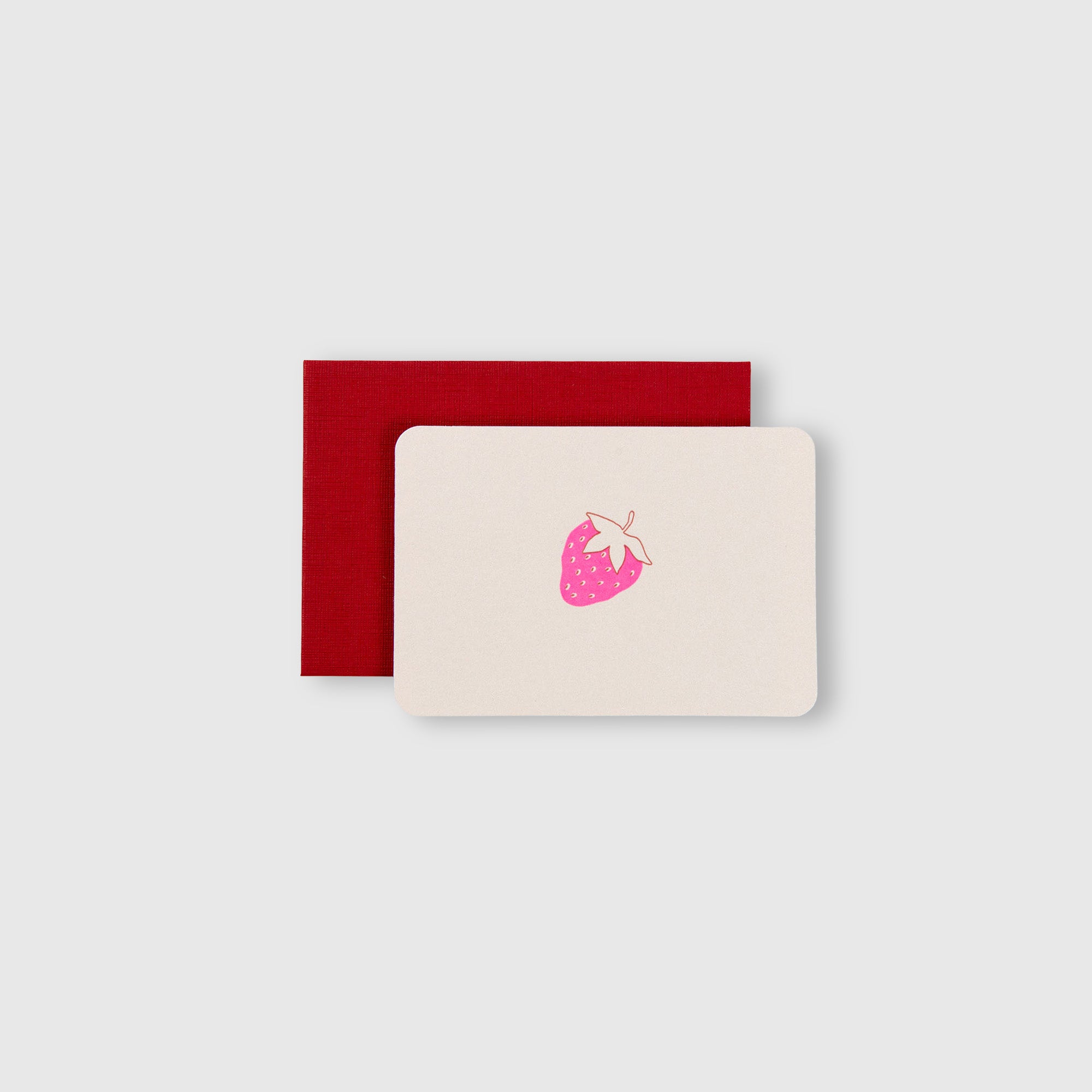 Eine cremefarbene „Erdbeere – Mini-Karte“ von Le Typographe mit einer rosa Erdbeer-Illustration liegt auf einem roten Umschlag vor einem schlichten hellgrauen Hintergrund.