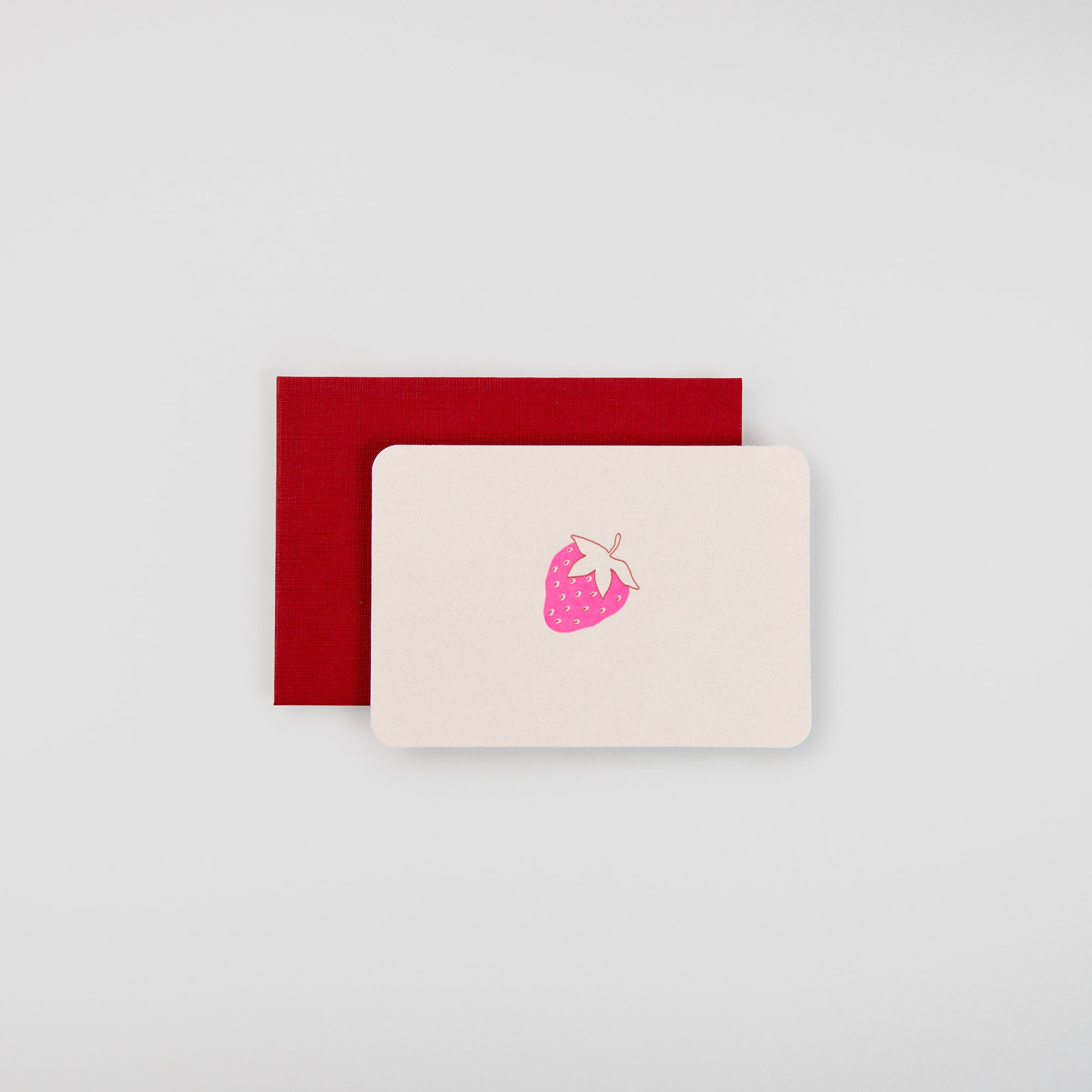 Die Erdbeere - Mini Karte von Le Typographe zeigt eine cremefarbene Karte mit einer rosa Erdbeer-Illustration auf einem roten Umschlag vor einem hellgrauen Hintergrund - perfekt, um die süße Essenz des Sommers einzufangen.