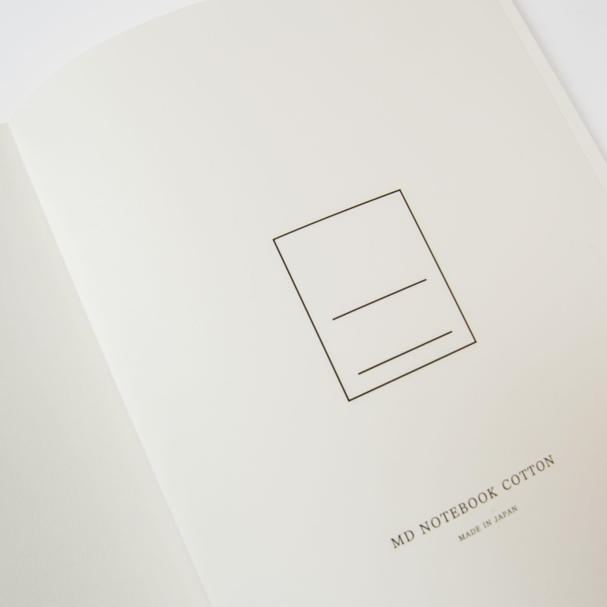 Nahaufnahme eines offenen Notizhefts mit Format von Midori, mit elegantem Aufdruck „MADE IN JAPAN“ auf einer cremefarbenen Seite. Eine minimalistische Skizze eines Rechtecks mit horizontalen Linien hebt die hochwertige Fadenbindung und das erstklassige MD Cotton Feinstpapier hervor.