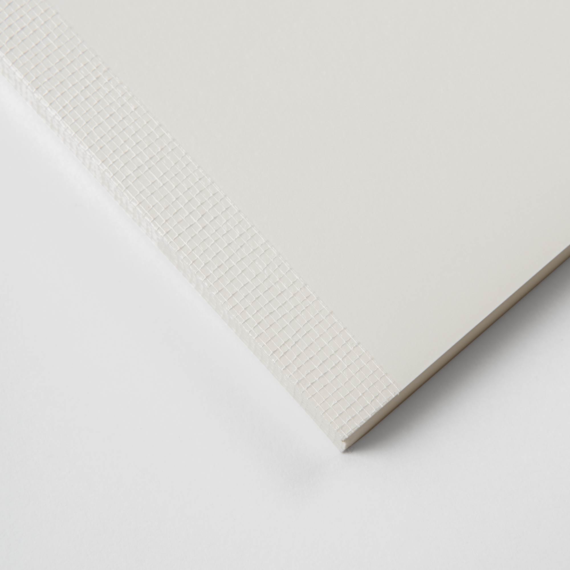 Nahaufnahme einer Ecke einer strukturierten weißen Oberfläche, wie bei Midoris „Ein Notizheft mit Format“ mit seinem karierten Muster. Eine dichtere Textur entlang einer Kante erzeugt einen Randeffekt, der den glatten Hauptbereich und den strukturierten Rand kontrastiert und an Fadenbindung erinnert.