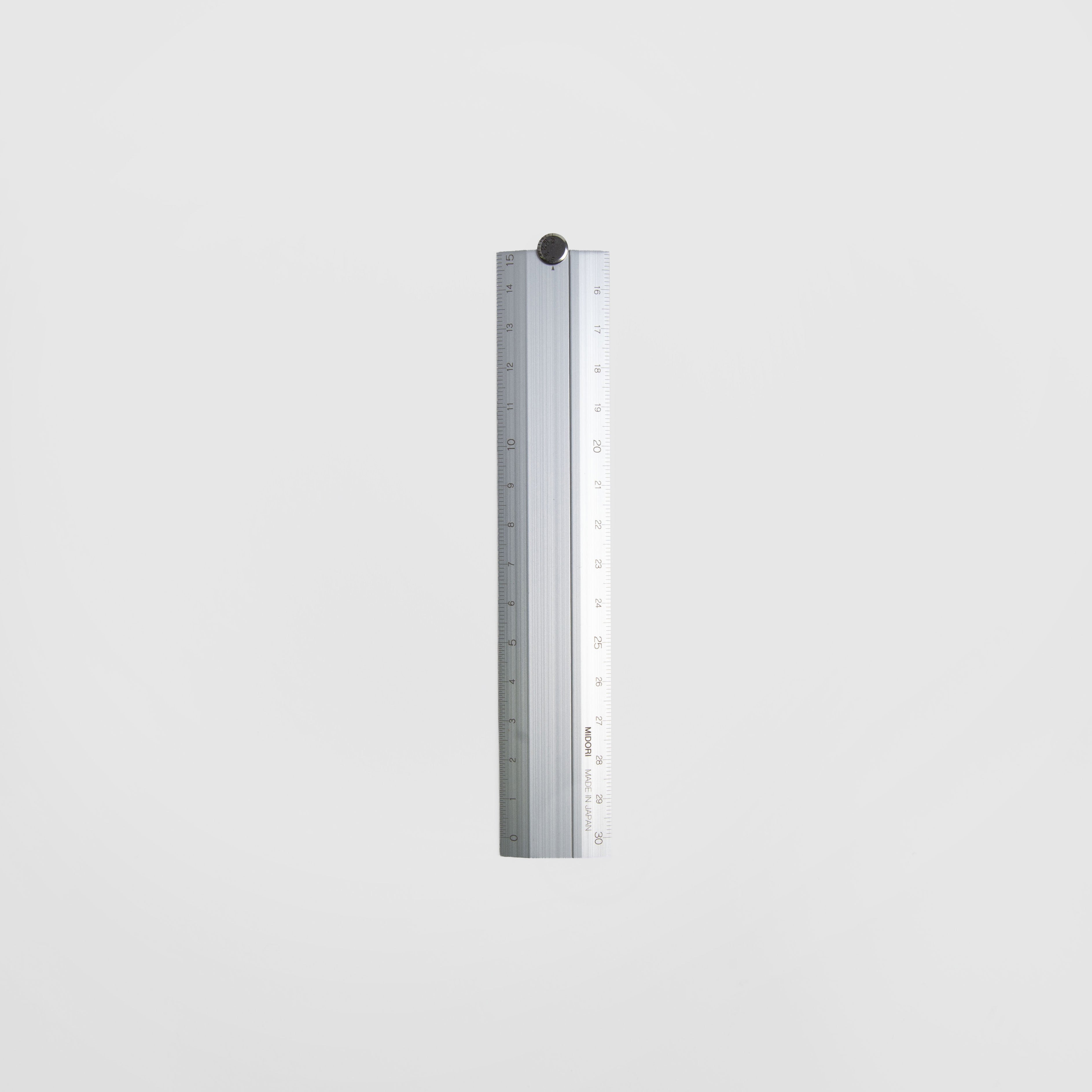 Das Midori Klapp-Lineal, ein silbernes Aluminiumlineal mit Zentimeter- und Inch-Markierungen, ist vertikal auf einem schlichten weißen Hintergrund abgebildet.
