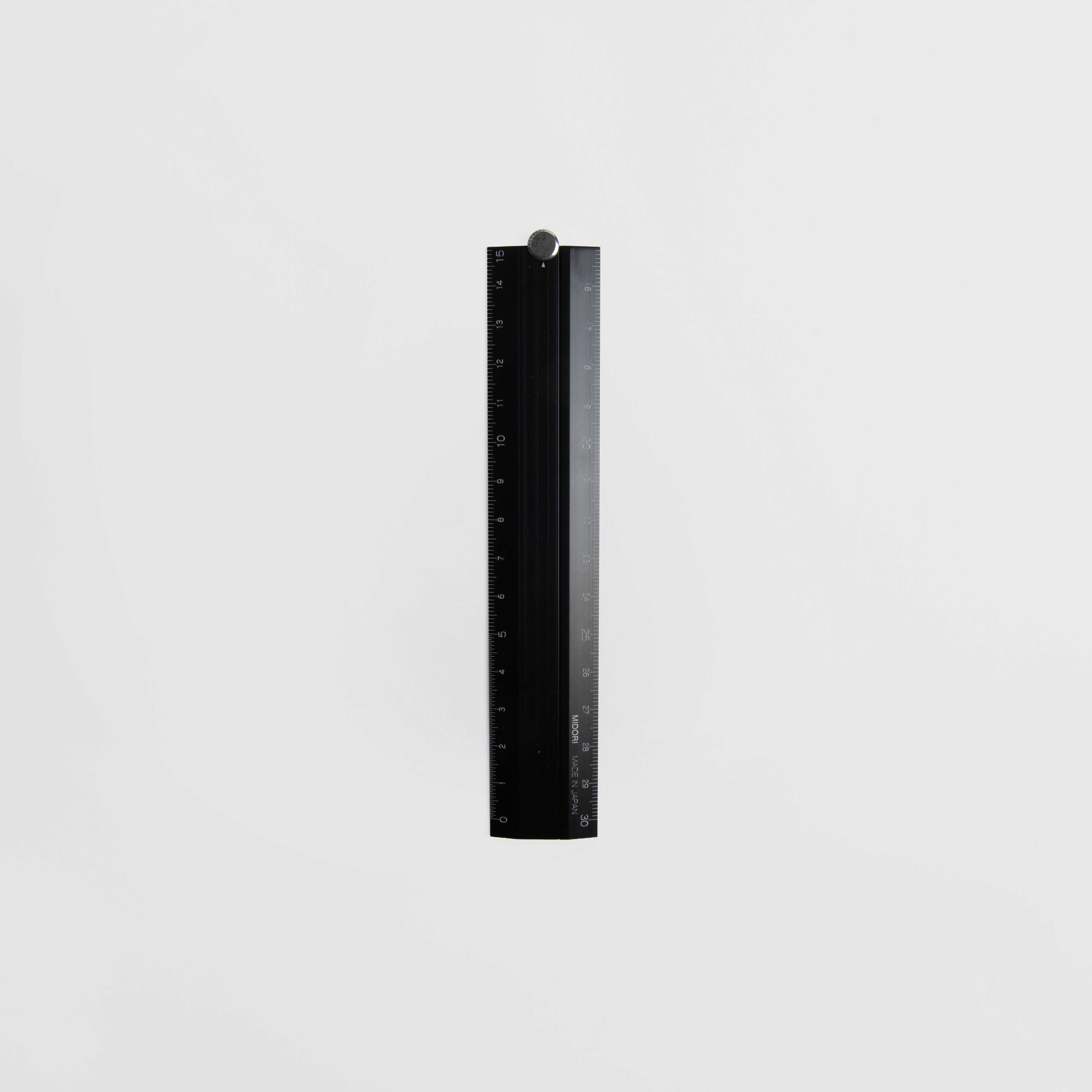 Das Midori Klapp-Lineal, ein schwarzes Aluminiumlineal von Midori mit deutlichen Messmarkierungen, steht senkrecht auf einem schlichten weißen Hintergrund.