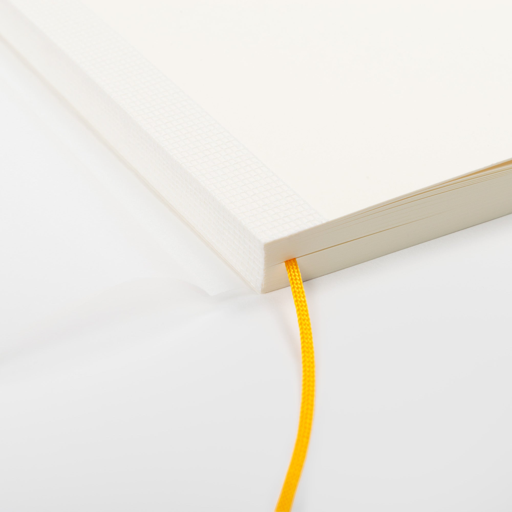 Eine Nahaufnahme eines aufgeschlagenen Midori MD Notizbuchs A5 mit cremefarbenen MD Papier Seiten, einem gelben Lesezeichen und einer haltbaren Fadenheftung, platziert auf einer weißen Oberfläche.
