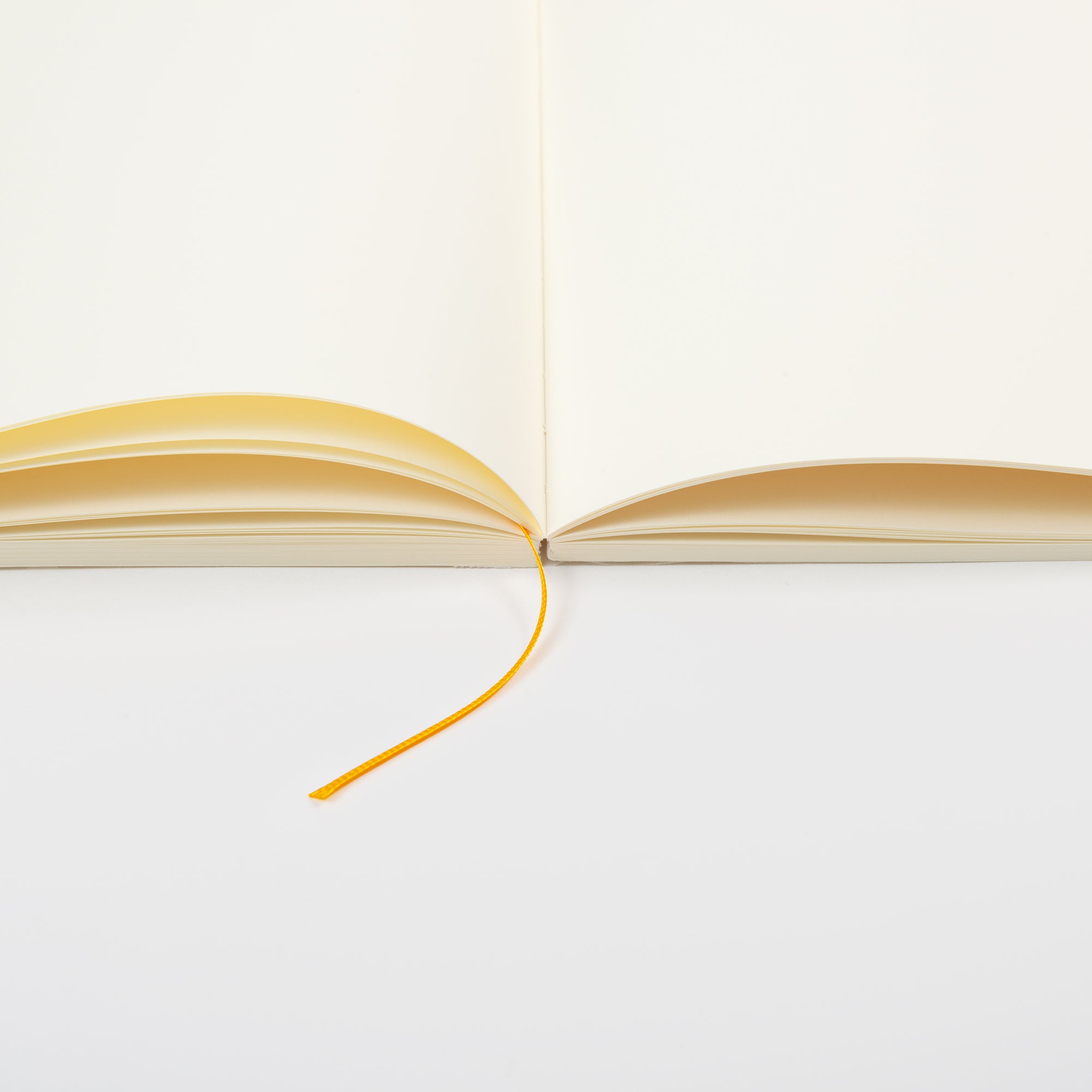 Ein aufgeschlagenes MD Notebook A5 von Midori mit cremefarbenem MD Papier liegt flach auf einer weißen Oberfläche. In der Mitte liegt ein Lesezeichen mit gelbem Band, das die elegante Fadenbindung zur Geltung bringt.