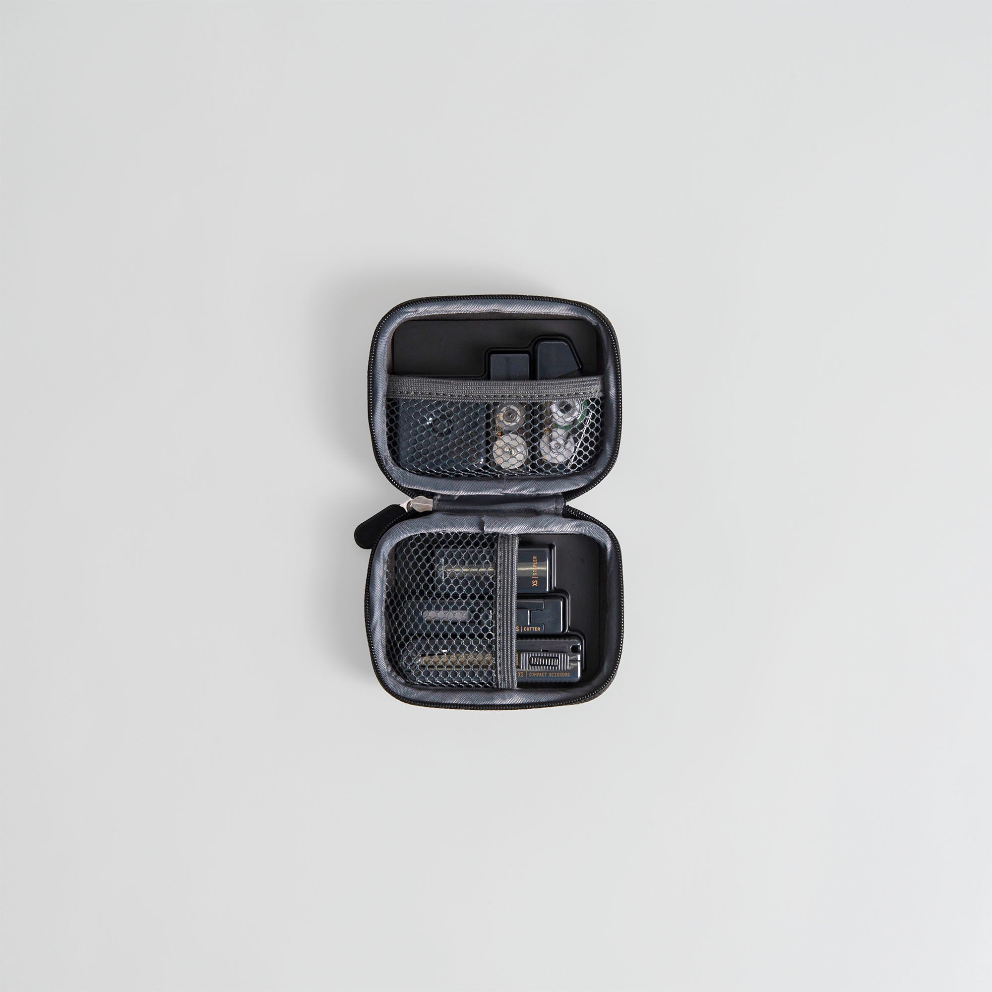 Ein kompaktes schwarzes Etui mit Reißverschluss, wie das Midori XS Stationery Kit von Midori, liegt offen auf einem weißen Hintergrund mit Netztaschen für Batterien, Speicherkarten und kleines Zubehör.