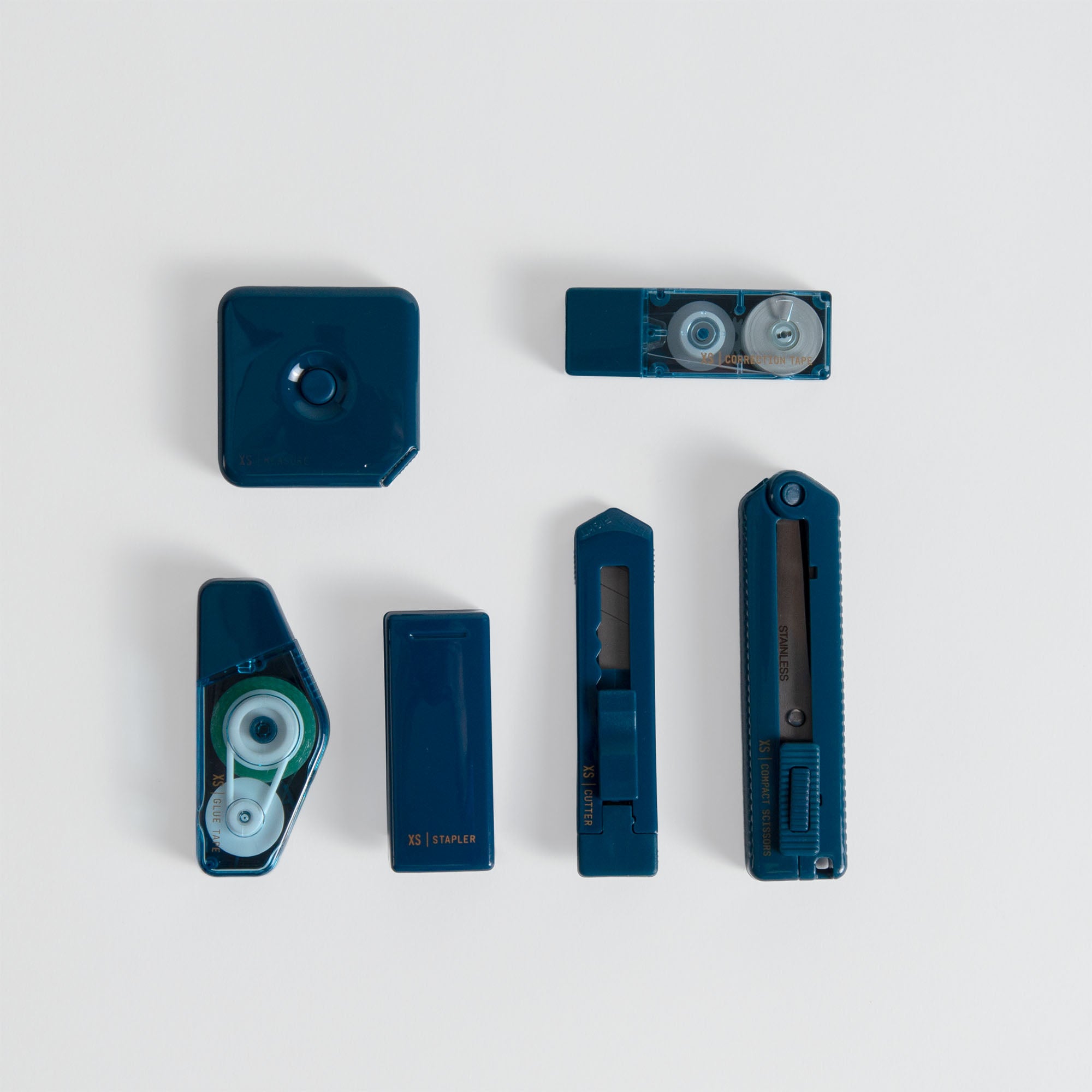 Sechs blaue Schreibtischutensilien aus dem Midori XS Stationery Kit von Midori - Hefter, Klebebandabroller und Universalmesser - sind in zwei Reihen auf einem schlichten weißen Hintergrund angeordnet und zeigen ein elegantes kompaktes Schreibtischset.