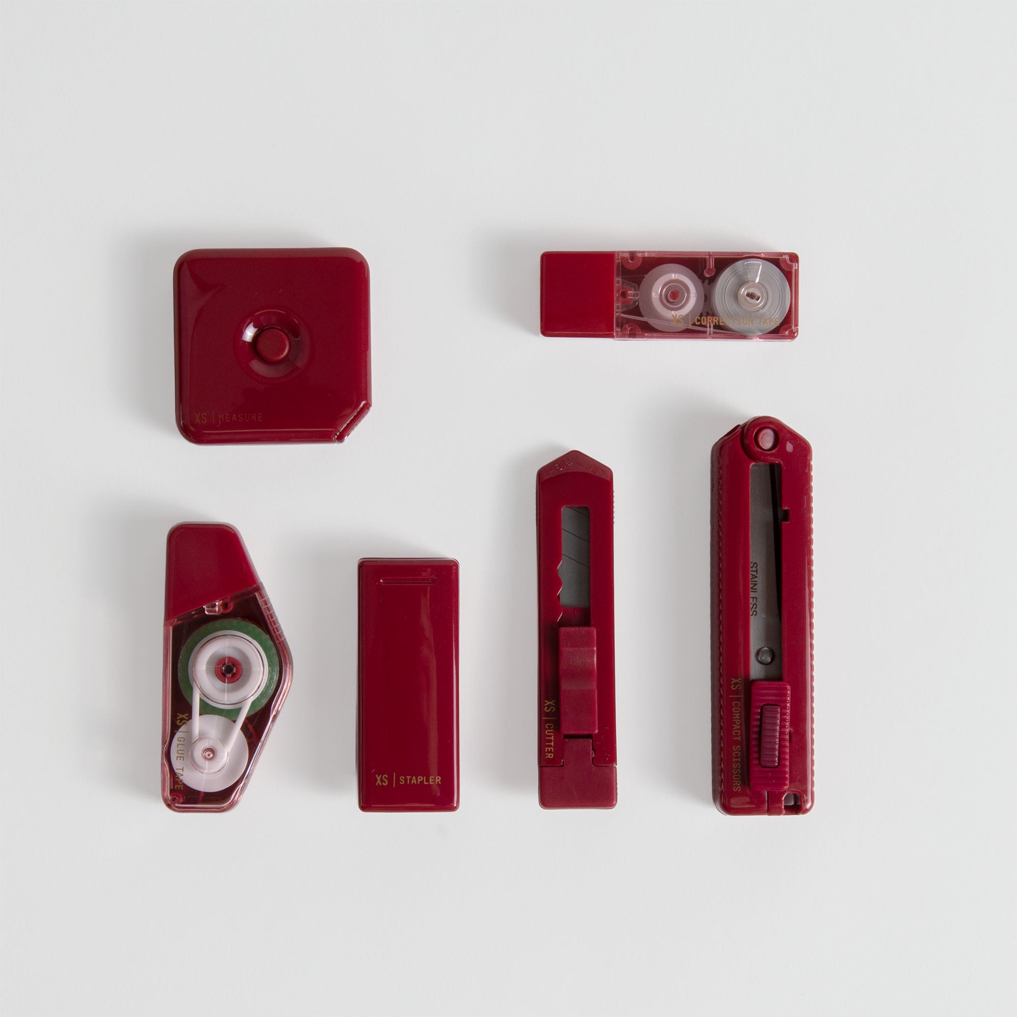 Sechs rote Midori XS Stationery Kit Werkzeuge, wie z.B. ein Hefter, ein Klebebandabroller und ein Universalmesser, sind ordentlich in zwei Dreierreihen auf einem weißen Hintergrund angeordnet.