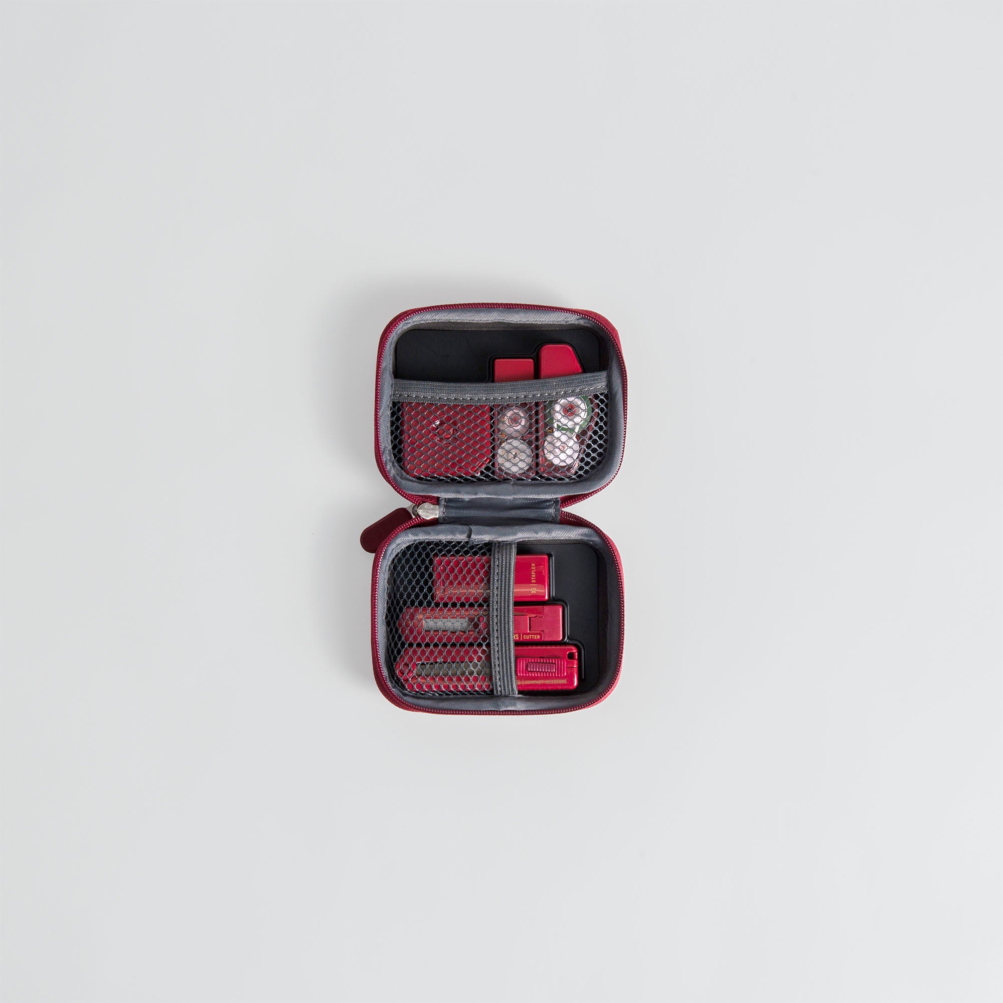 Ein kompaktes rotes Midori XS Stationery Kit von Midori mit Netztaschen, die kleine rote und durchsichtige Behälter enthalten, auf einem schlichten weißen Hintergrund.