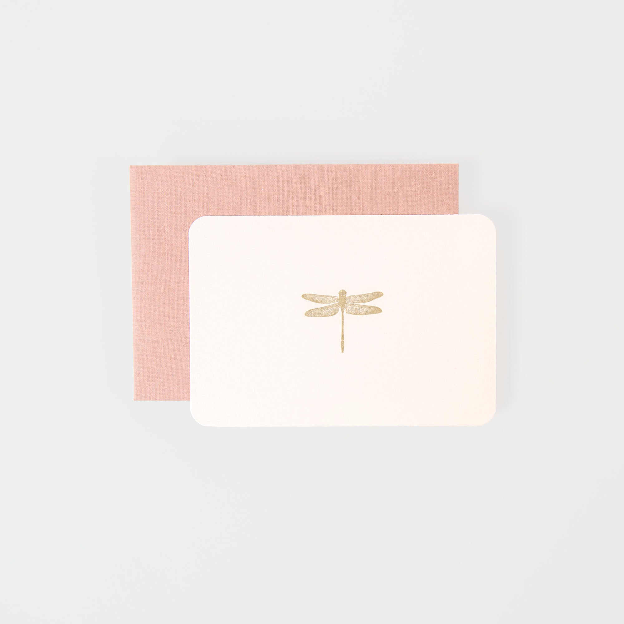 Die Le Typographe Libelle - Minikarte verfügt über ein minimalistisches Design mit einer goldenen Libelle auf weißem Hintergrund, gepaart mit einem pastellrosa Umschlag auf hellgrauer Oberfläche.
