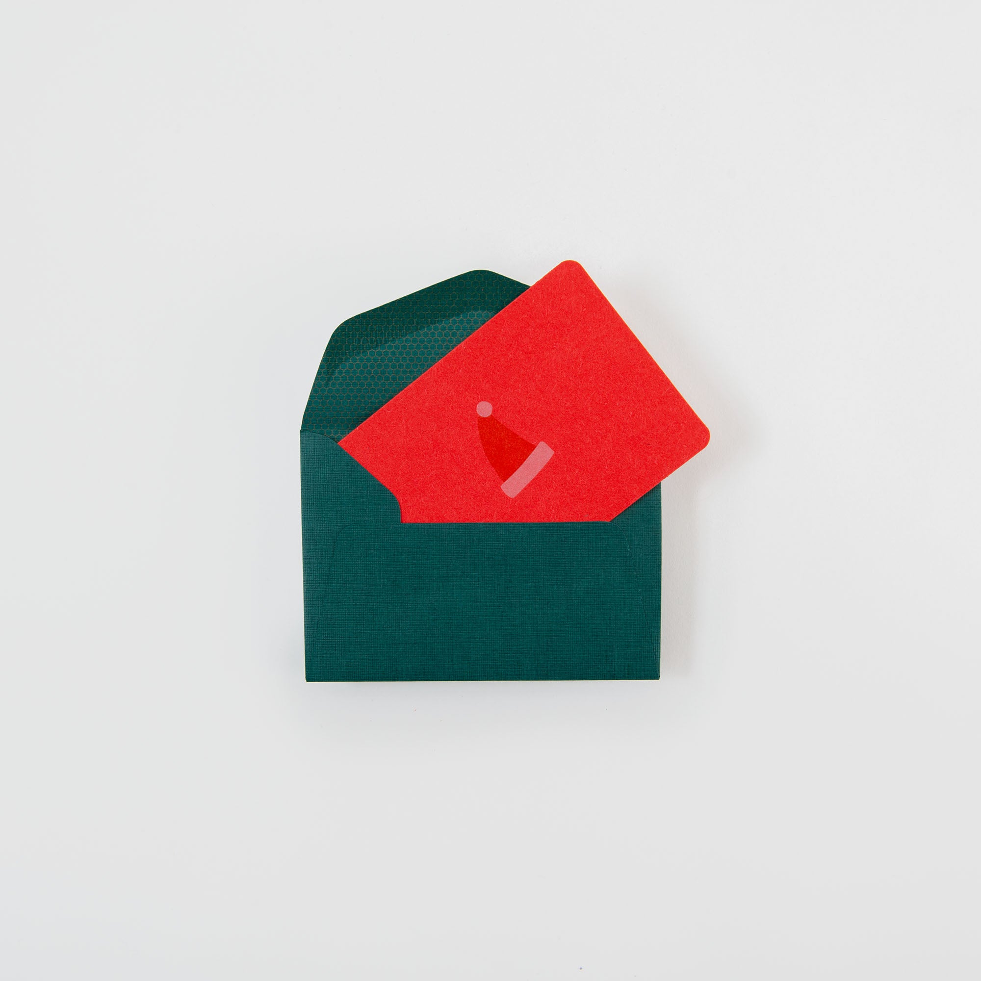 In einem grünen Umschlag steckt die Nikolausmütze - Mini Karte von Le Typographe mit einer schlichten Nikolausmütze. Diese festliche rote Karte ist perfekt für die Saison und ein Muss für Letterpress-Karten-Fans. Vor einem strahlend weißen Hintergrund.