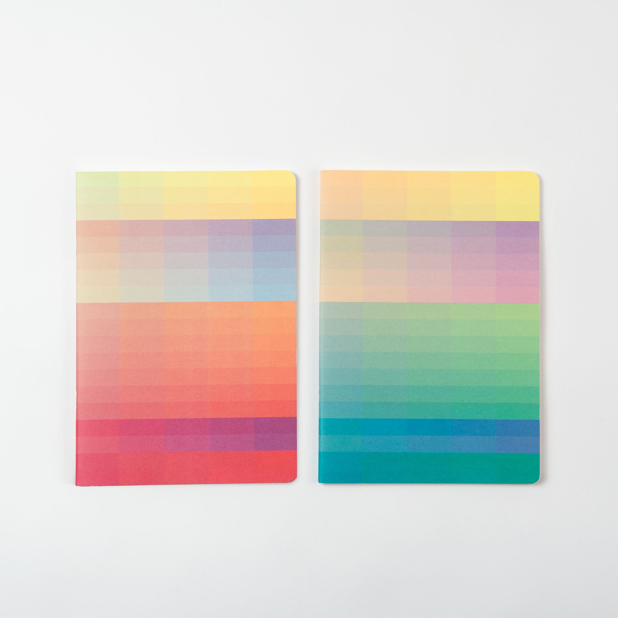 Die Notizhefte der Glitch Edition von paperlux.store umfassen zwei Notizbücher mit lebendigen, farbenfrohen Farbverlaufscovern. Das Design wechselt fließend von Rot und Orange oben zu Blau und Grün unten und erzeugt so einen glitchartigen Effekt auf einem schlichten, hellen Hintergrund.