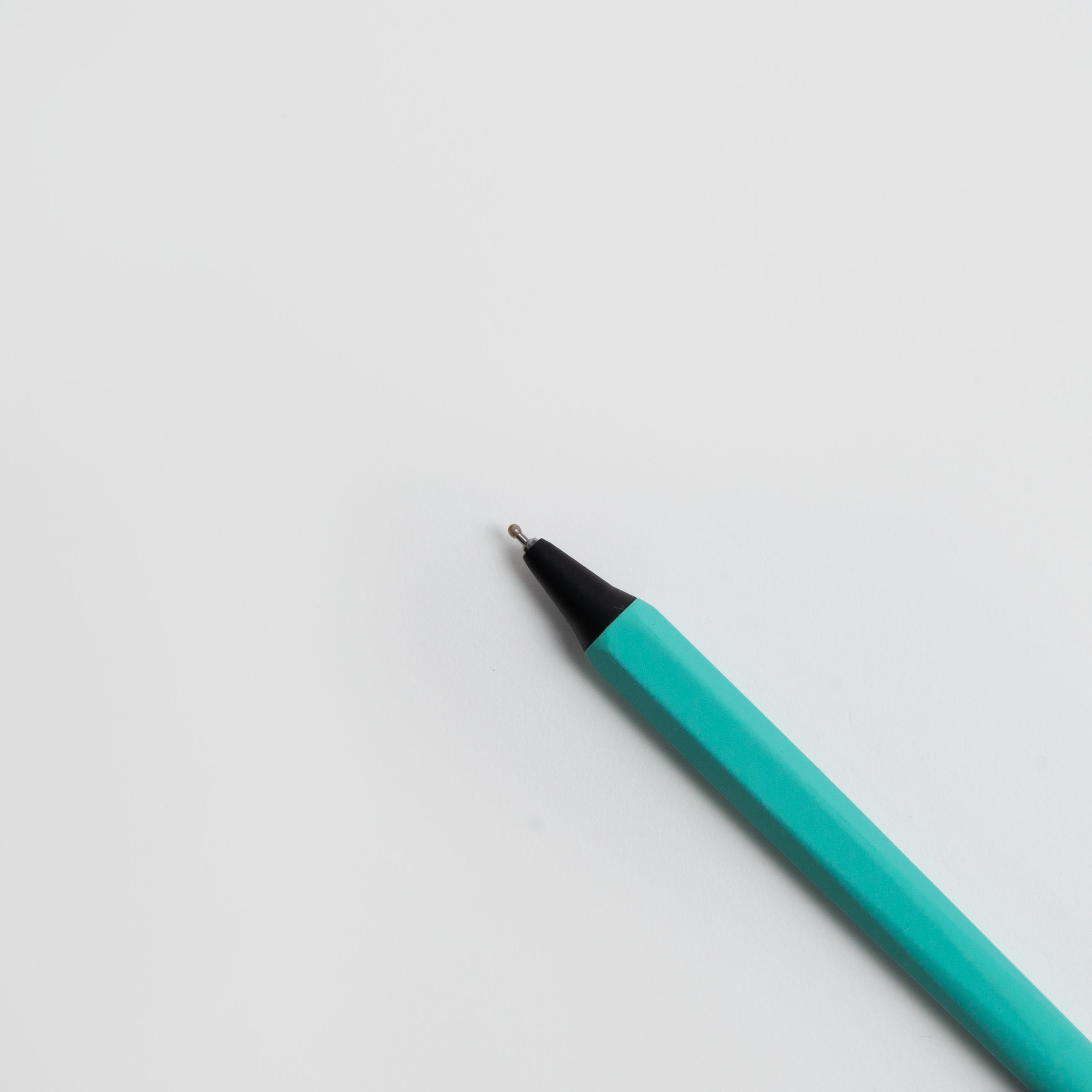 Ein türkisfarbener OHTO GS02 Gelschreiber - japanischer Gelstift von Marks Europe mit schwarzer Spitze liegt schräg auf einer weißen Fläche und zielt auf die obere rechte Ecke des Bildes.