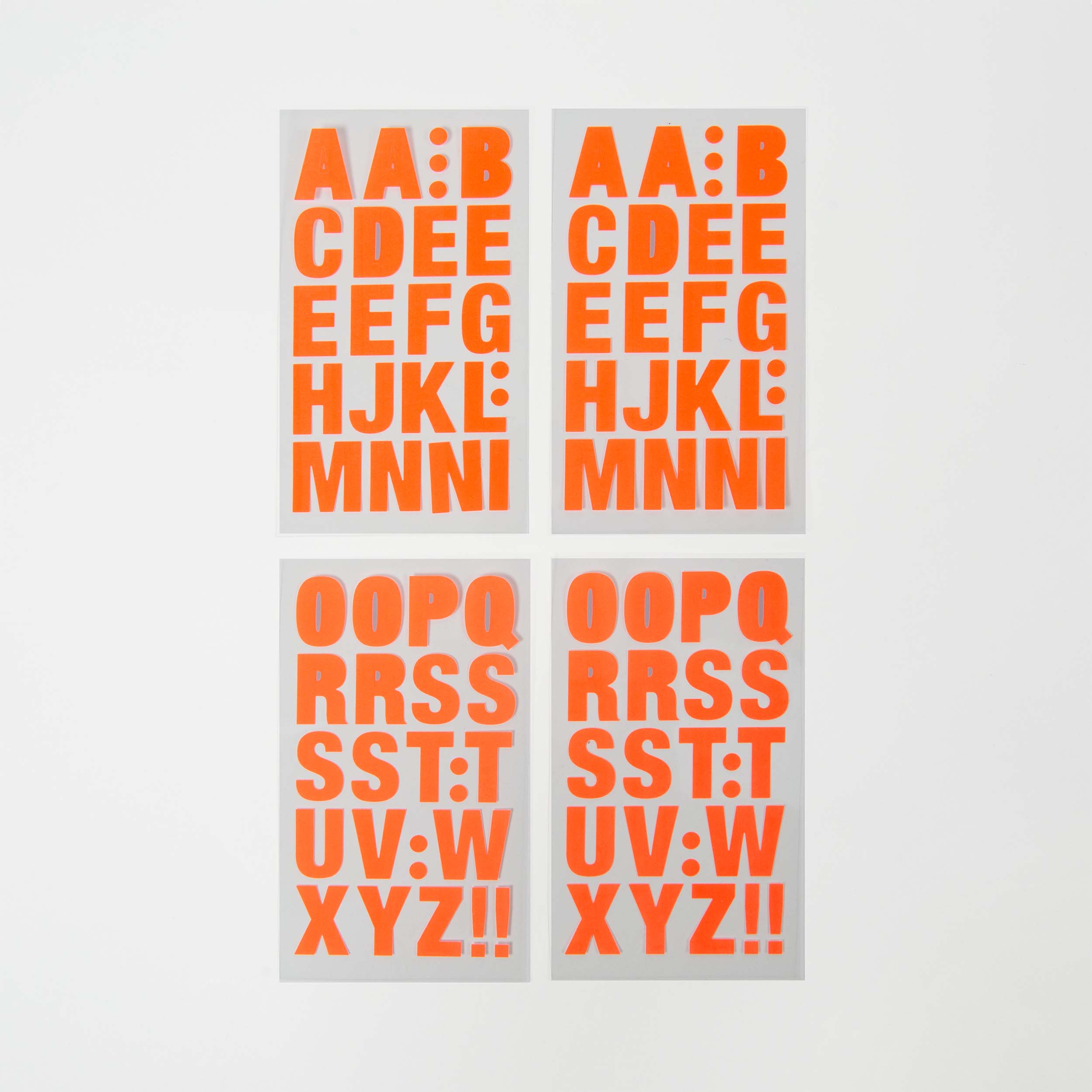 Die selbstklebenden Buchstaben von Paper Poetry bestehen aus vier weißen Blättern mit kräftigen, leuchtend orangefarbenen Buchstaben. Auf den beiden oberen Blättern steht „AA:BBCDEEFGHIJKLMNNI“, auf den beiden unteren „OOPQRSSTTUV:WXYZ!!“. Alle Großbuchstaben füllen die Blätter vollständig aus und lassen keinen Platz für Farbvarianten.